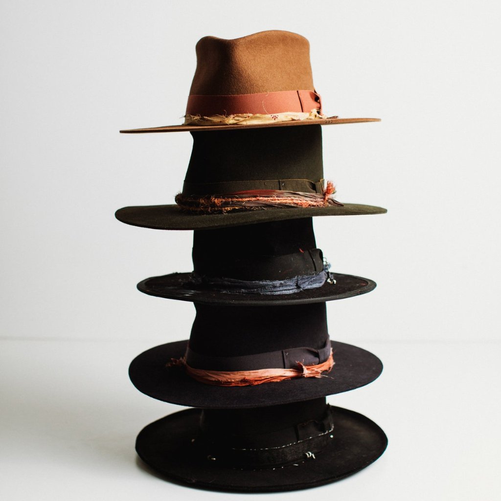Stack of PHYLLi felt hats in deep, moody colourways, Caramel, Artichoke, Black and Navy, styled with vibrant trims and dramatic silhouettes.