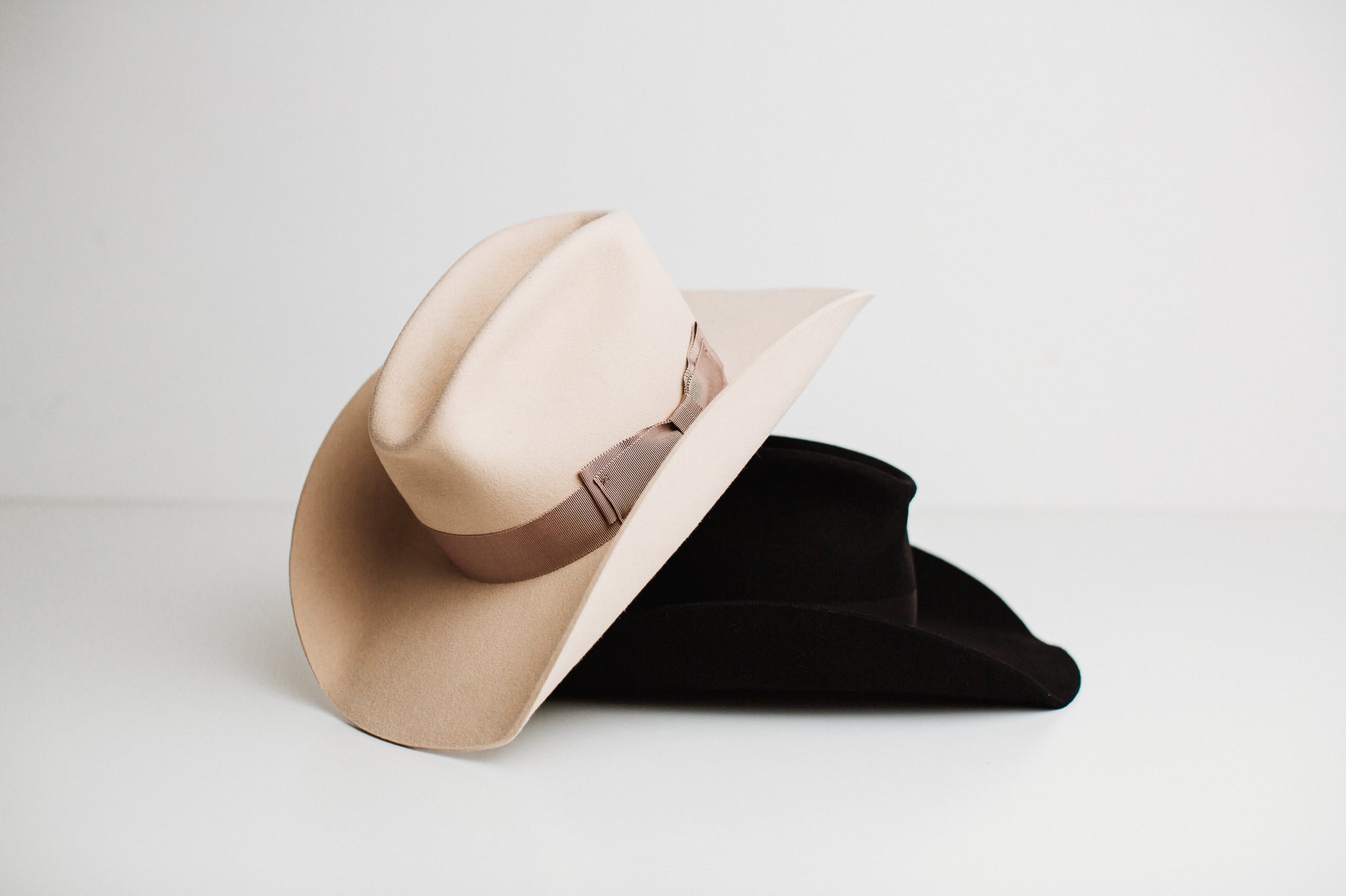 Two custom cowboy hats from PHYLLi Designs, one beige and one black, shaped in the style called The Plains