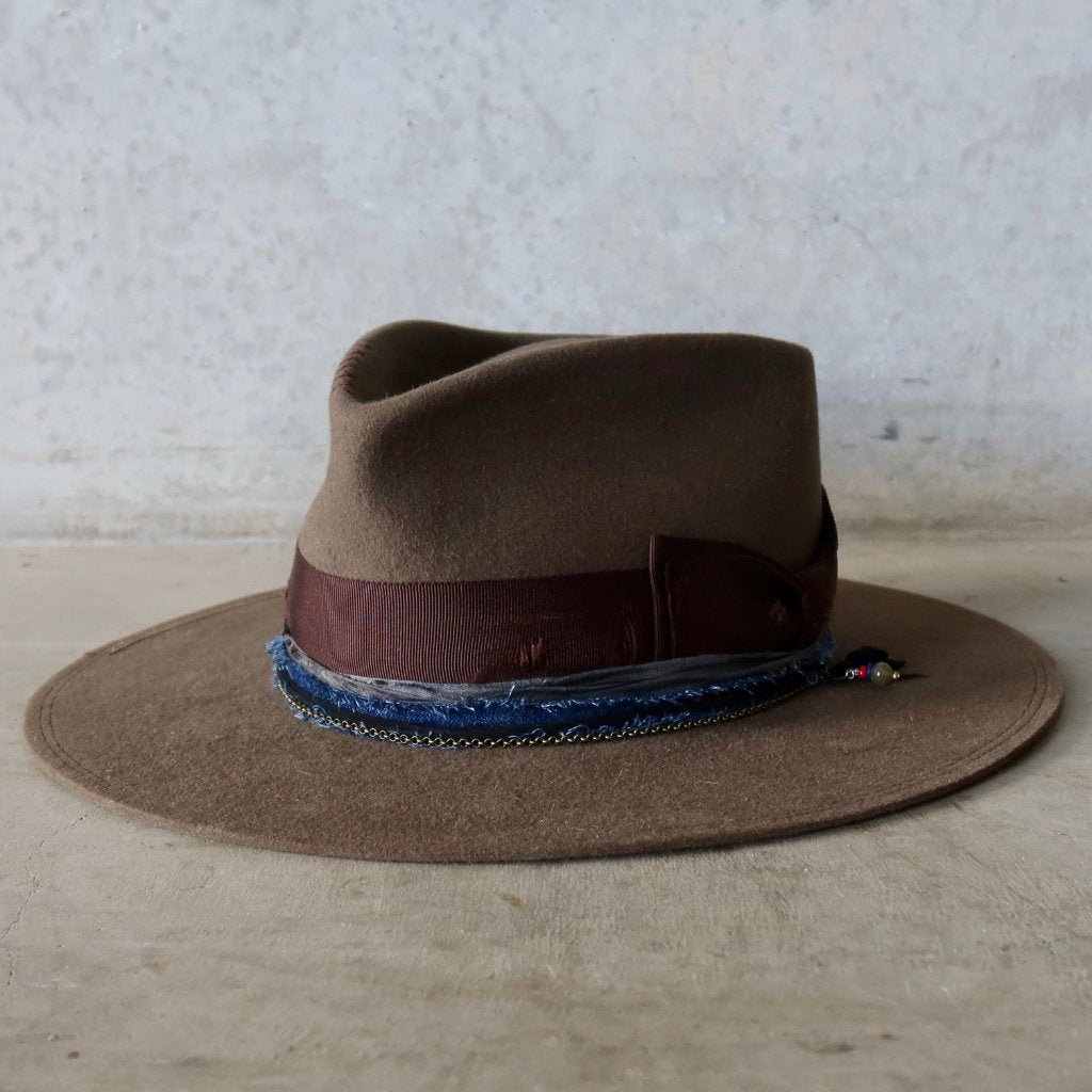 Olive felt hat with layered hat band in ribbon, silk, denim and chain, handcrafted by PHYLLi Designs and photographed against a raw concrete backdrop
