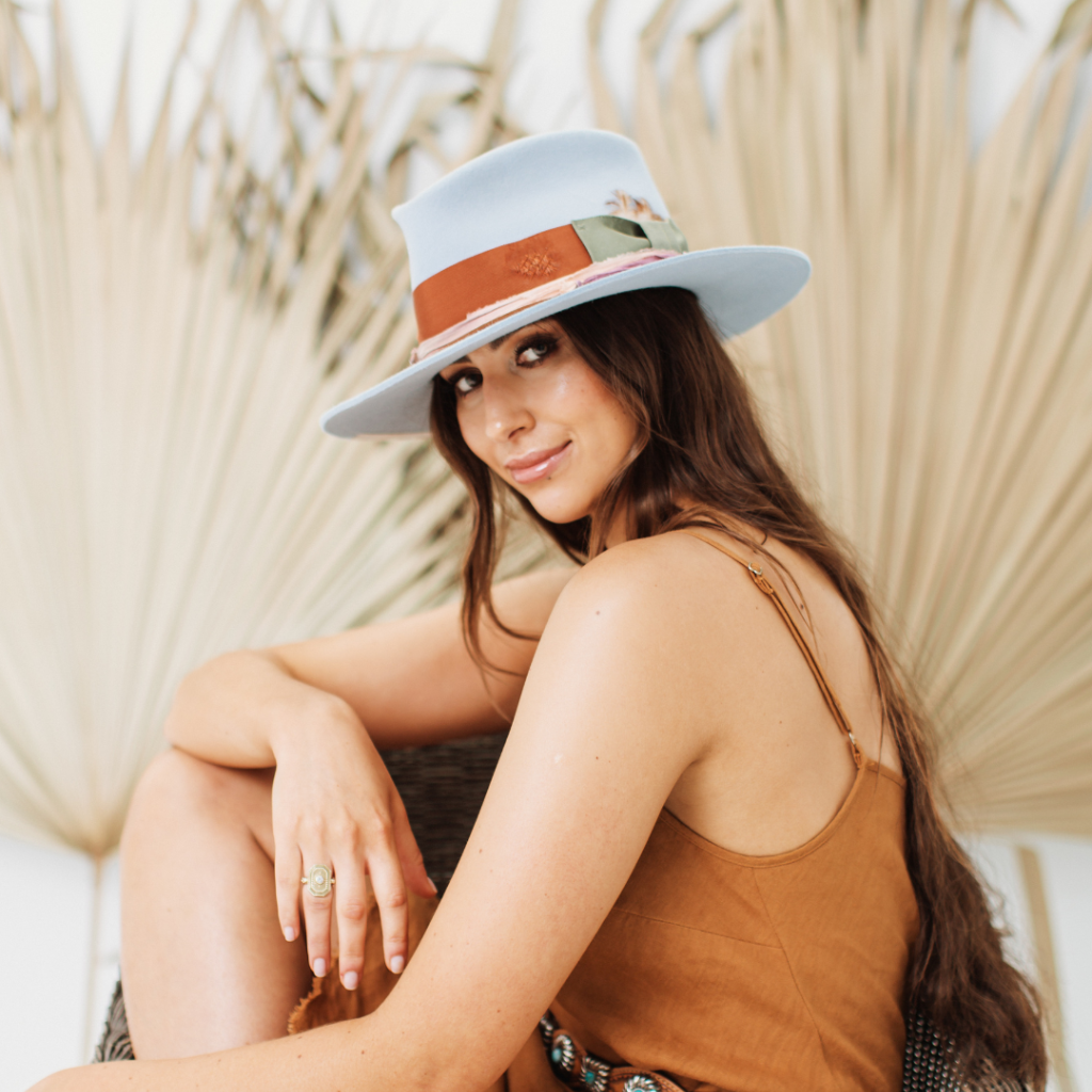 Girl sitting in a chair wearing a crystal blue felt hat featuring layered trims in rust, pink silk and oil green - a PHYLLi best seller