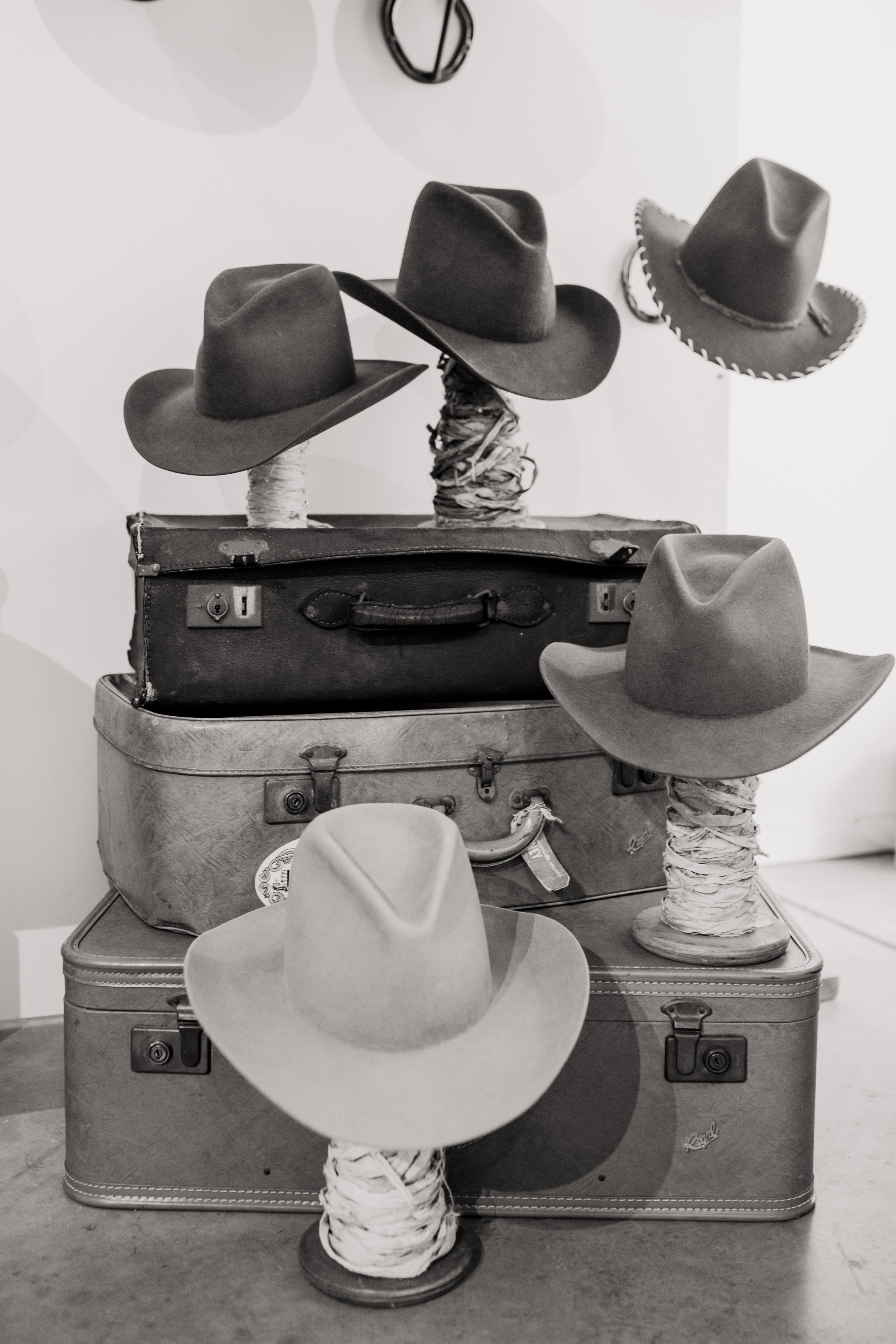 Stacked felt hats in classic western shapes styled on vintage suitcase, PHYLLi Hat Bar custom hat experience.