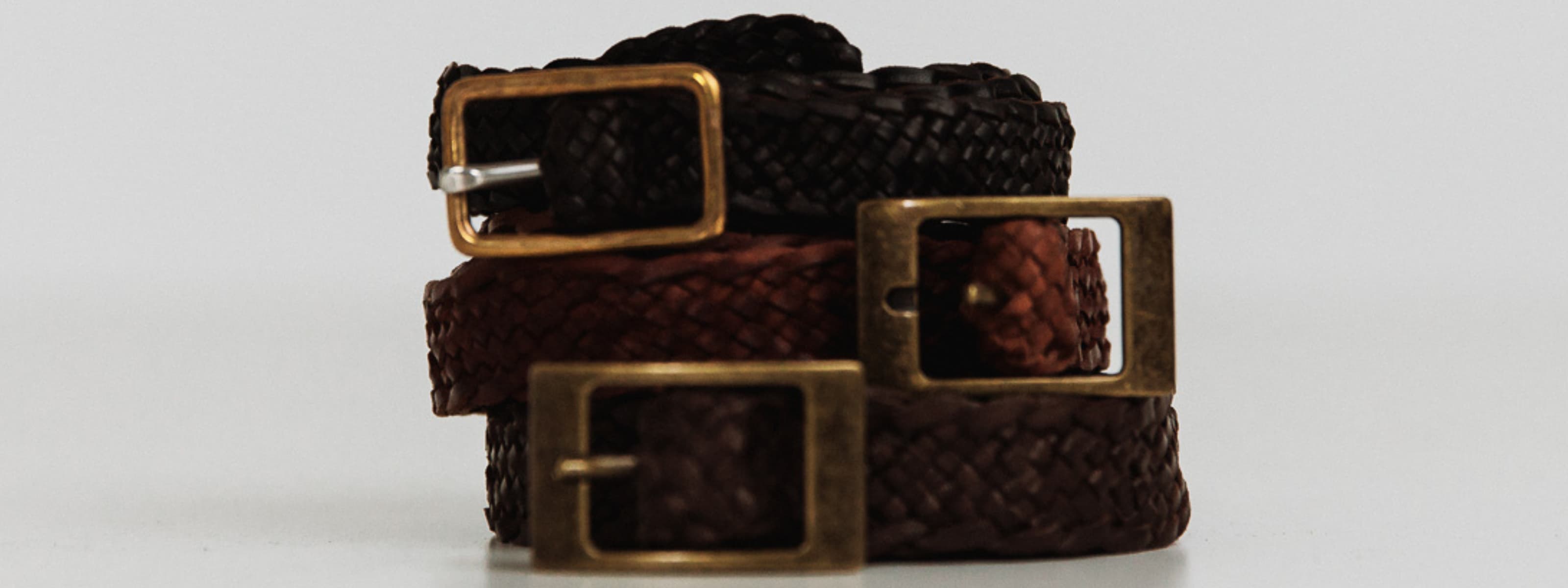 Three woven belts with brass buckles on a light gray background
