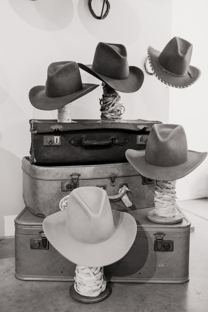 Stack of vintage suitcases with cowboy hats on top in a black and white photo.