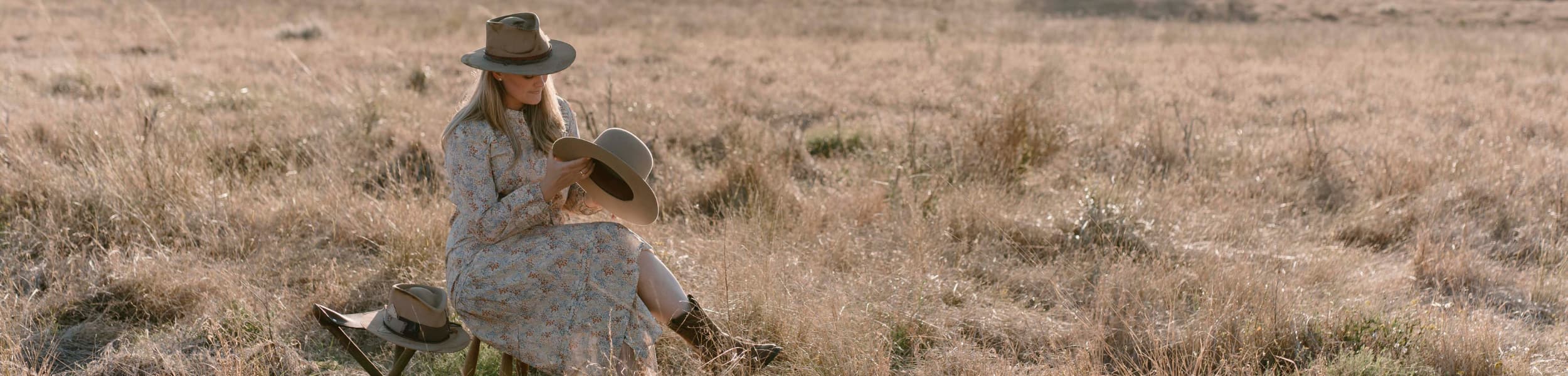 Banner image of Laura Hall sitting in a field whilst stitching a handmade hat