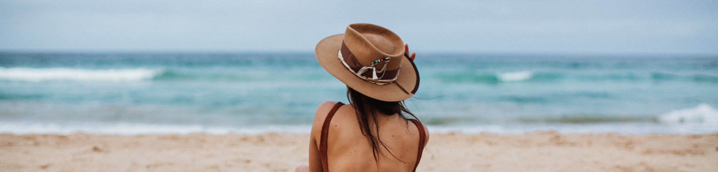 Girl wearing a camel felt hat by PHYLLi Designs, sitting on the sand looking out to the ocean