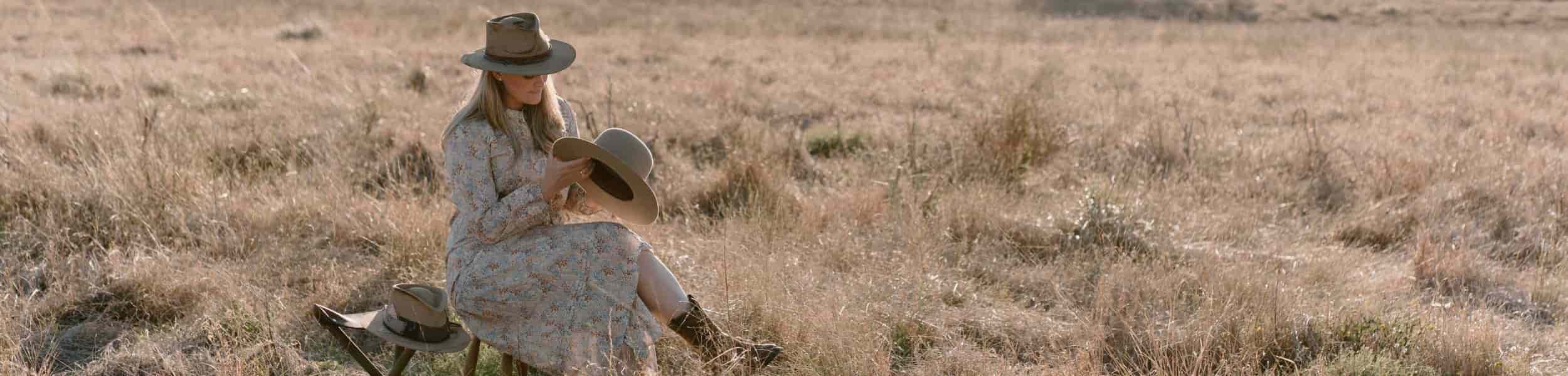 Laura Hall sitting on a bench in a field, wearing a hat and dress.
