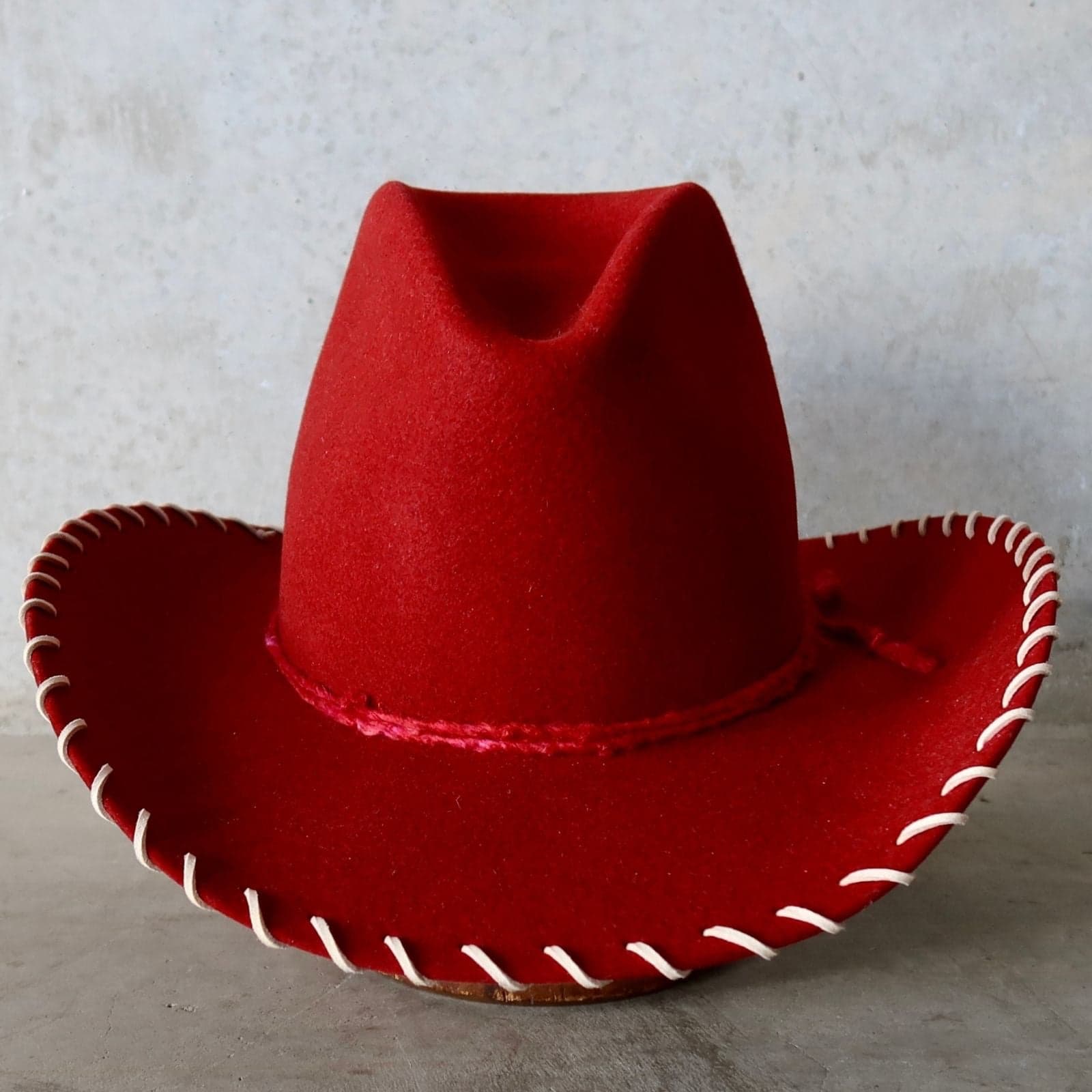Red cowboy hat with white stitching on a gray background