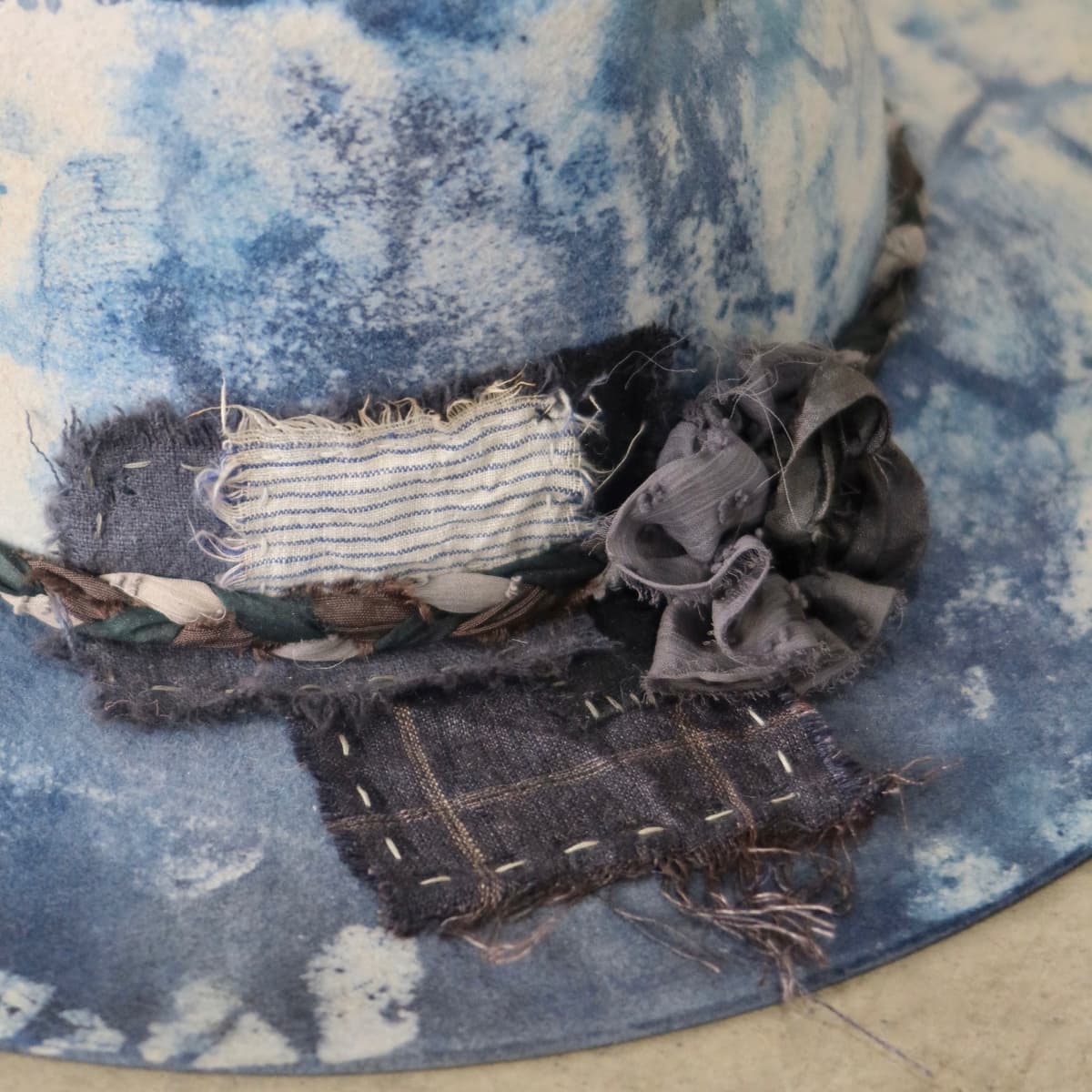 Close up detail of the Aizome Limited Edition felt hat showing wabi sabi linen and cotton patchwork with hand stitching and sari silk lapel bloom.