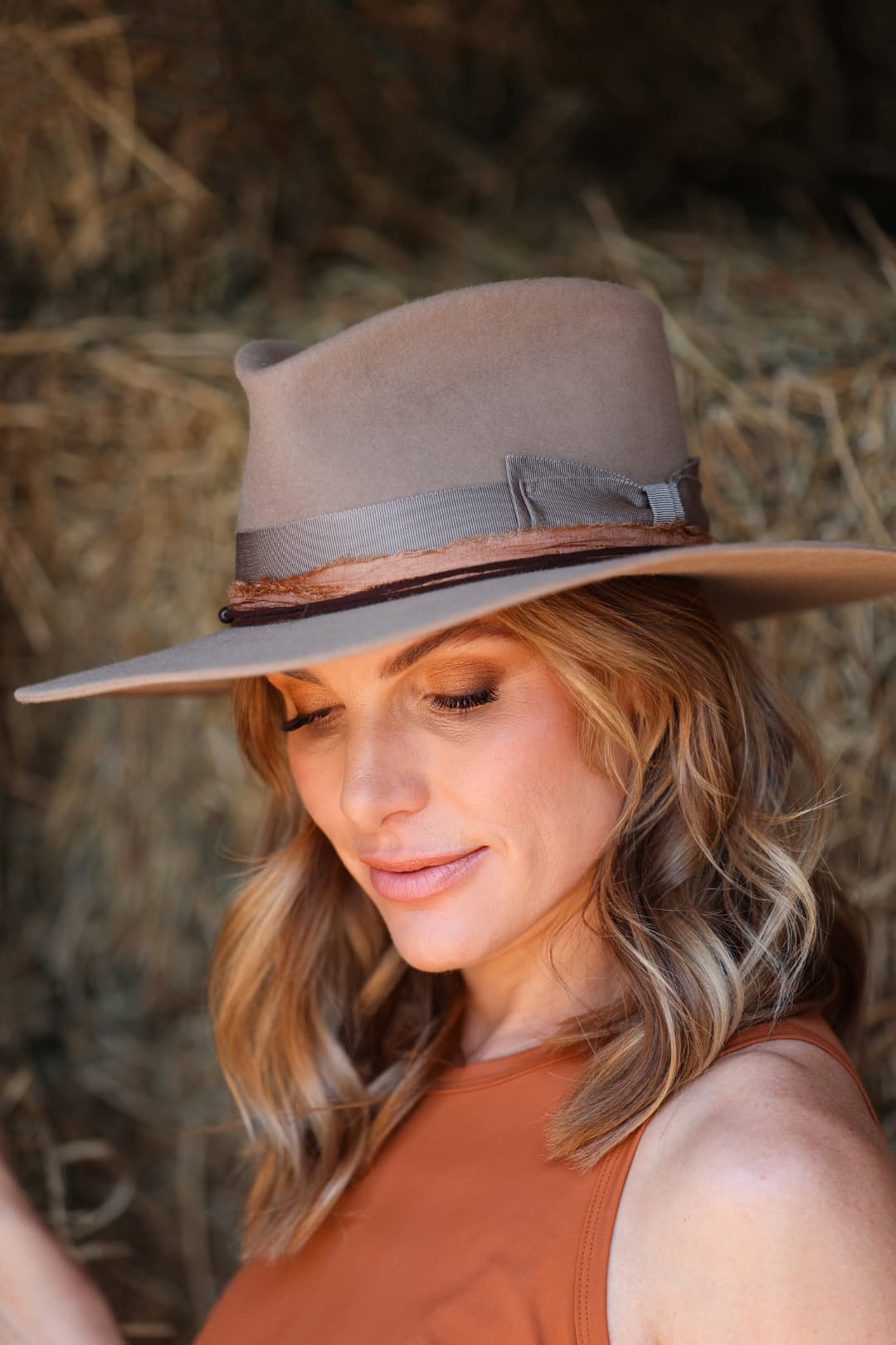 Close up woman wearing the Alexander Camel felt hat by PHYLLi Designs with copper sari silk trim while standing beside hay bales.