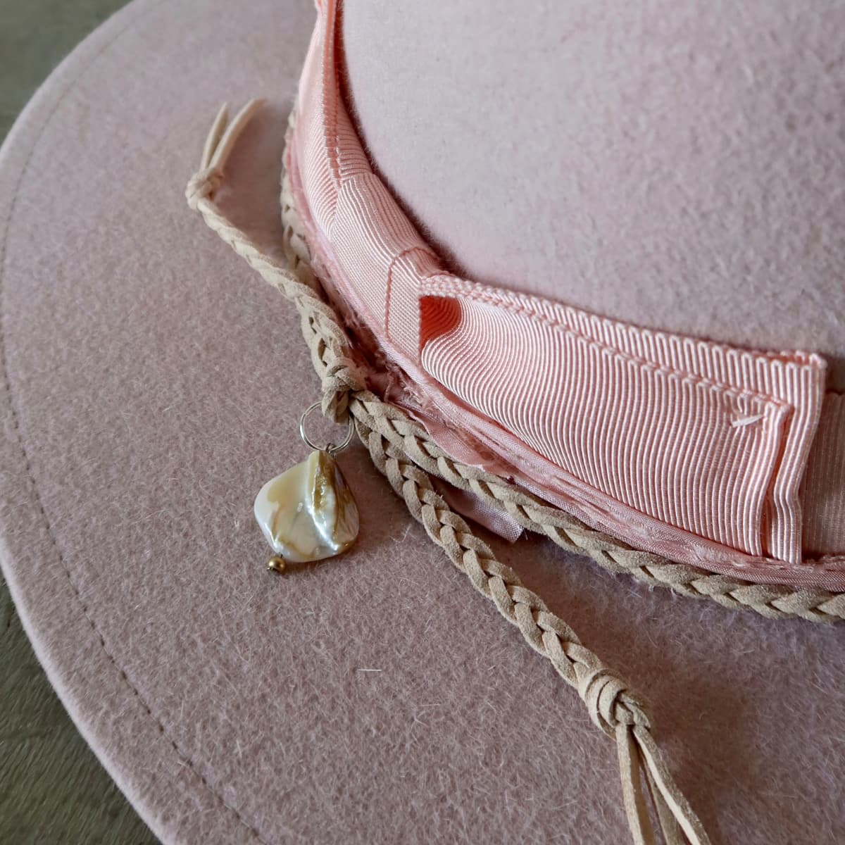 Close up detail of the Argyle Limited Edition felt hat showing plaited nude suede string with rough pearl pendant charm.