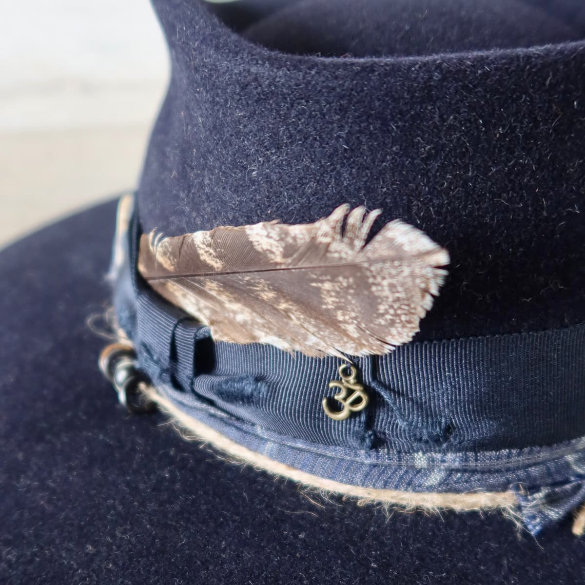Close up detail of the Armadale felt hat showing fallen feather tucked into the hat band and bronze ohm symbol detail.