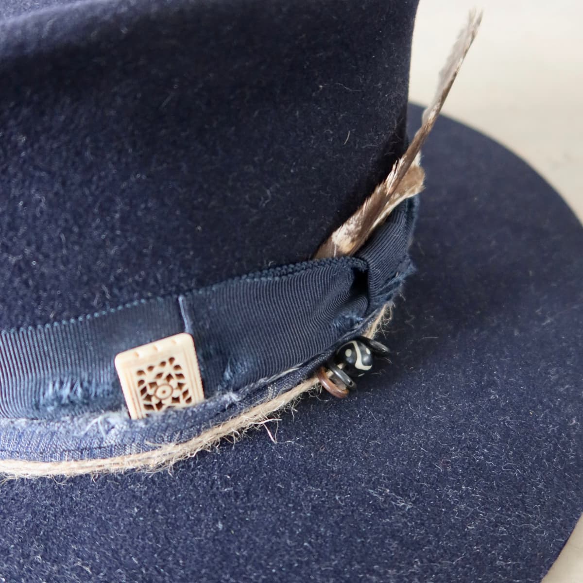 Close up detail of the Armadale felt hat showing rectangular bone bead charm and distressed grosgrain bow band.