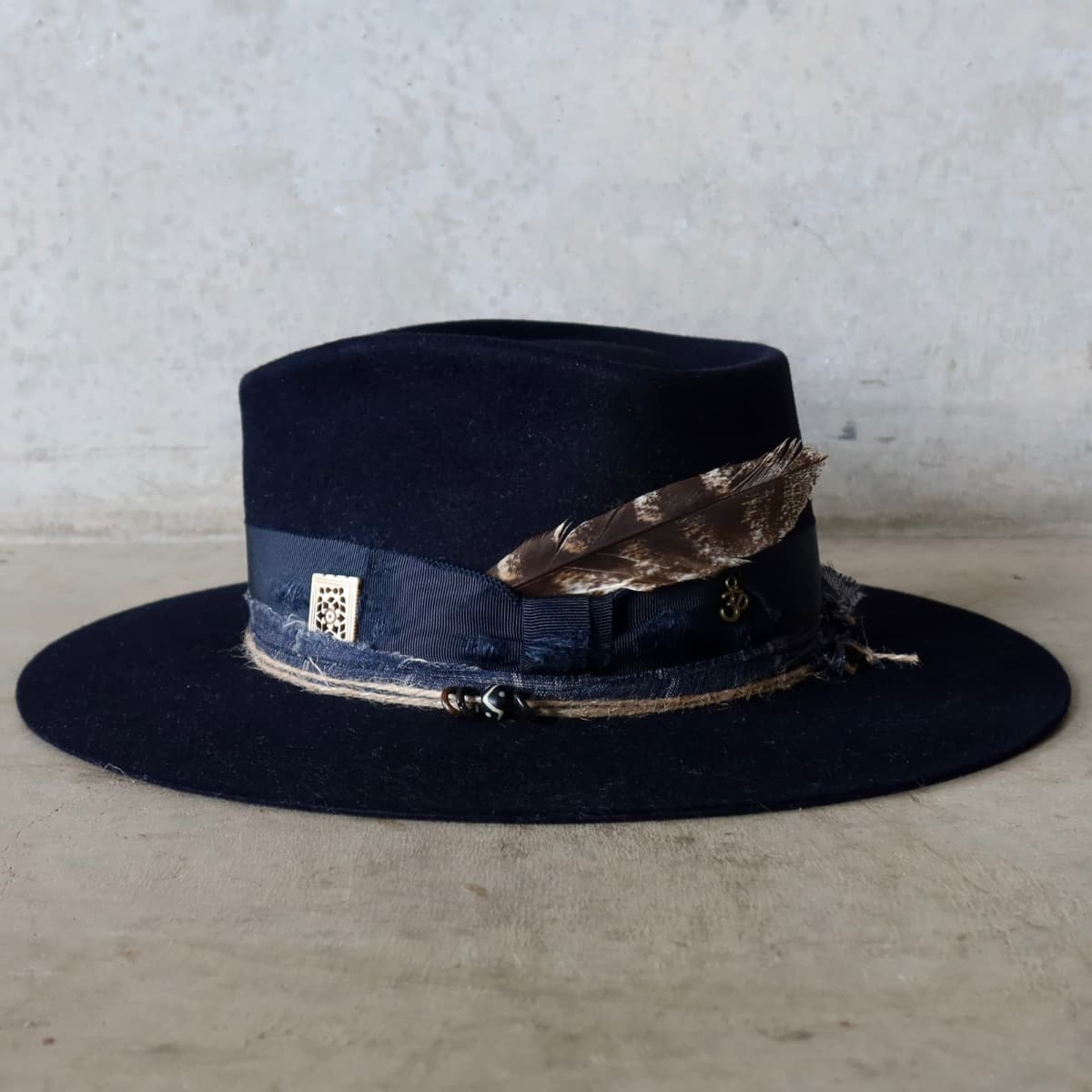 Front left angle of the Dark Navy felt hat Armadale by PHYLLi Designs with fallen feather, bone bead charm and antique bronze Ohm symbol charm.