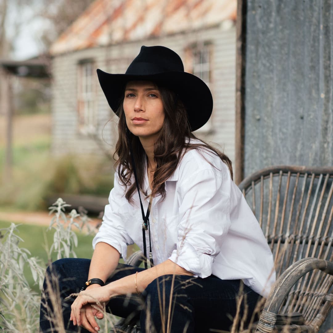 Female model wearing the black felt cowboy hat B&W Wheeler by PHYLLi Designs with black Japanese grosgrain band in a rustic countryside setting.
