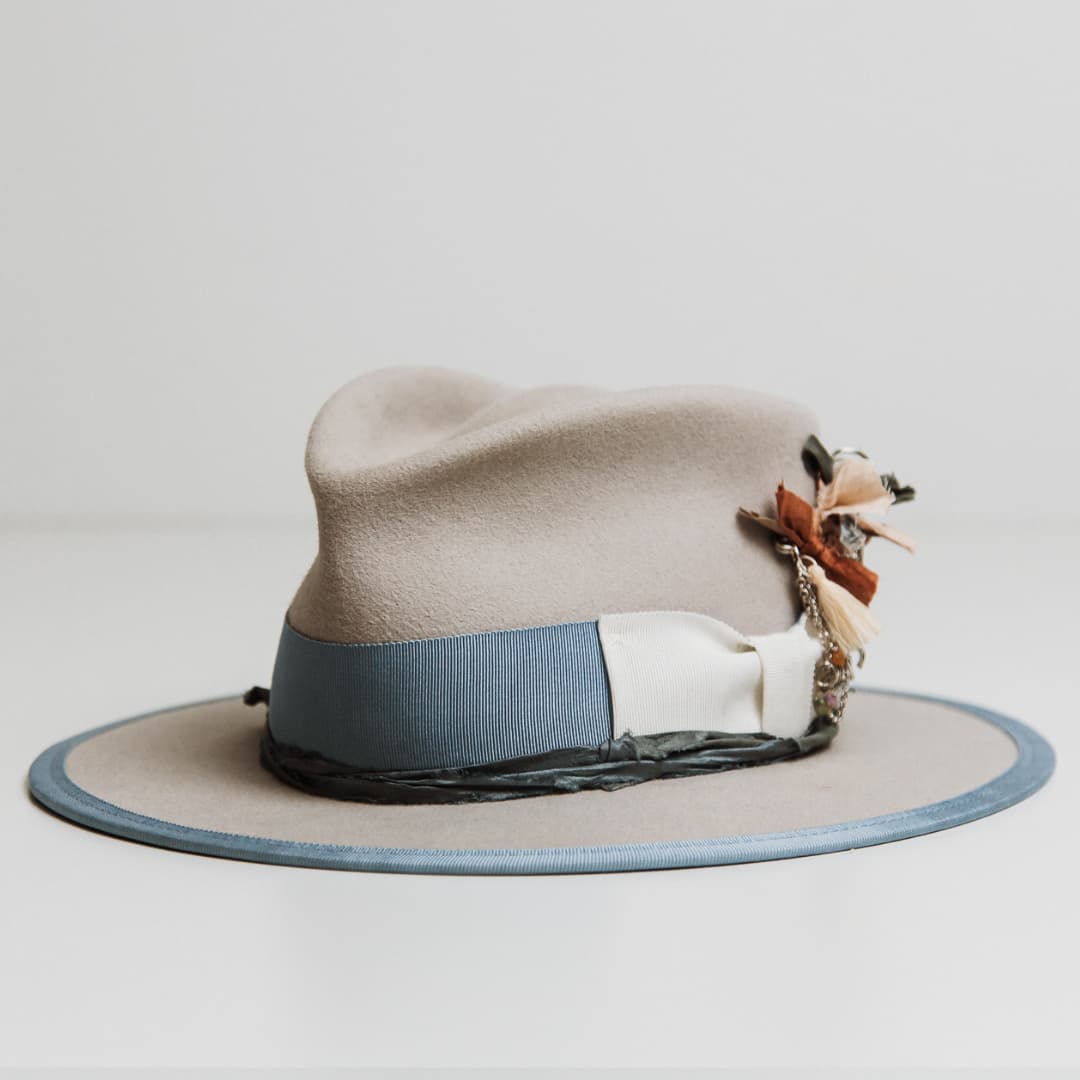Bleu de France felt hat showing Cornflower grosgrain band, Ivory bow and silver chunky hat pin with tassel and charms.
