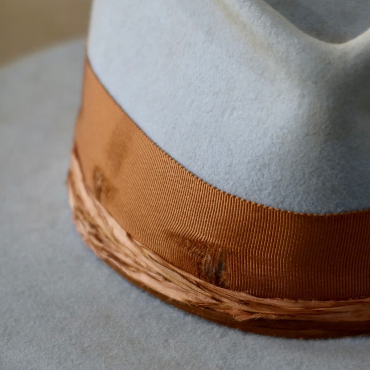Close up detail of the Blue Bloom felt hat showing distressed copper grosgrain band with worn patch and tan suede string wrap.