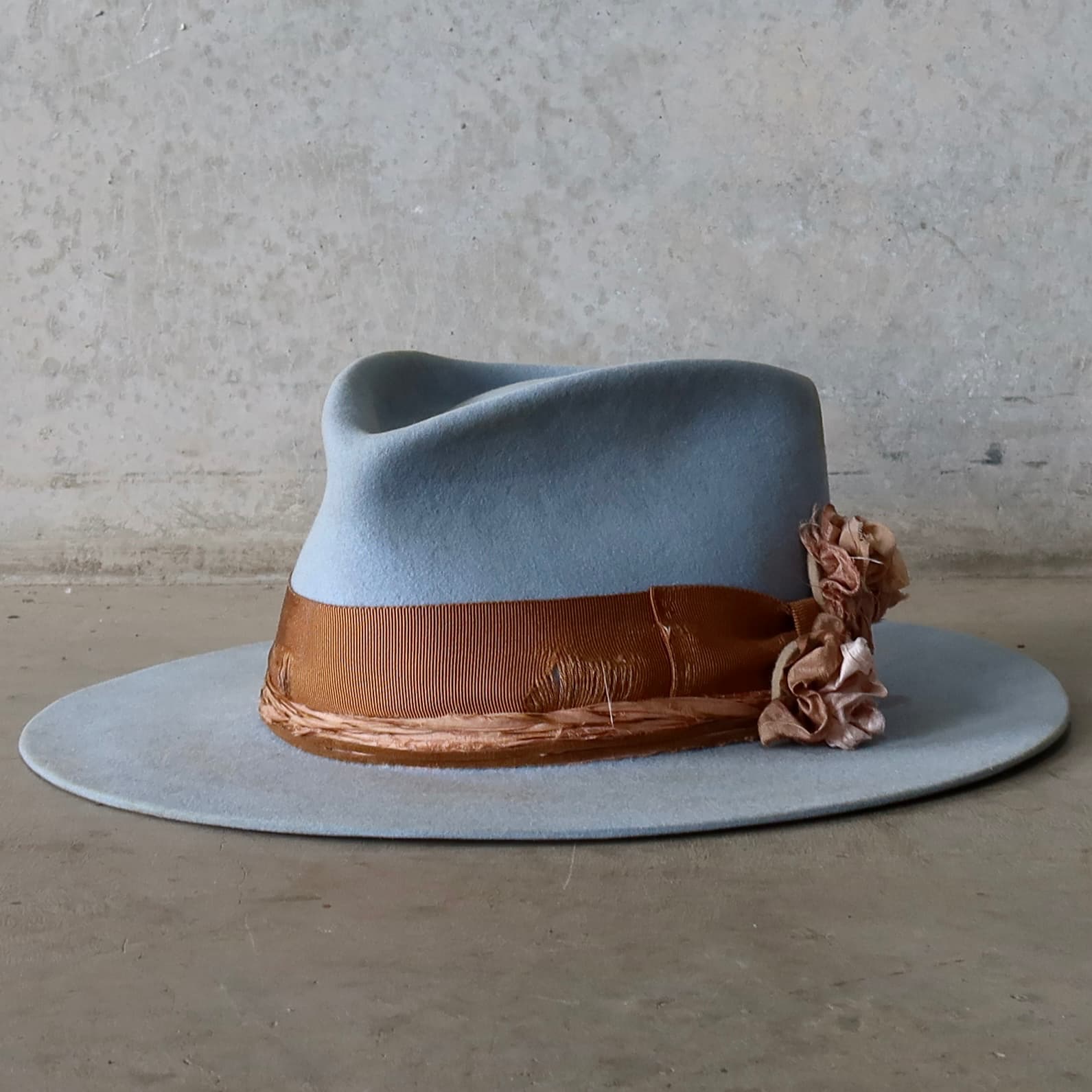 Front left angle of the crystal blue felt hat Blue Bloom by PHYLLi Designs with distressed copper grosgrain band, tan suede string and sari silk Lapel Bloom.