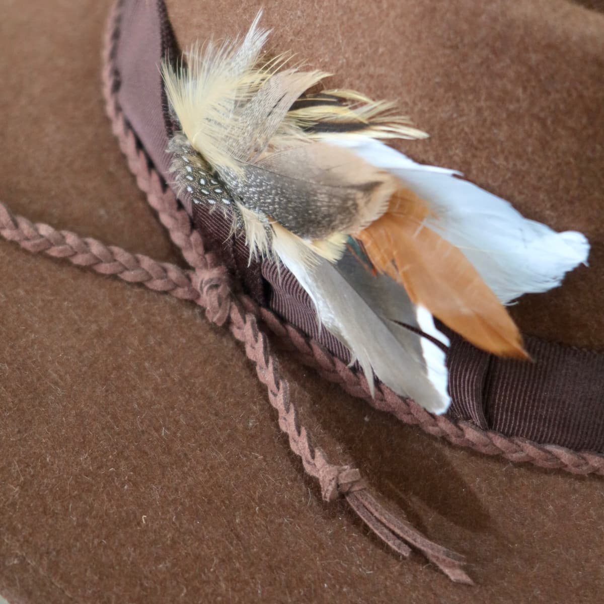 Close up detail of the Botero felt hat showing plaited chocolate suede string trim.