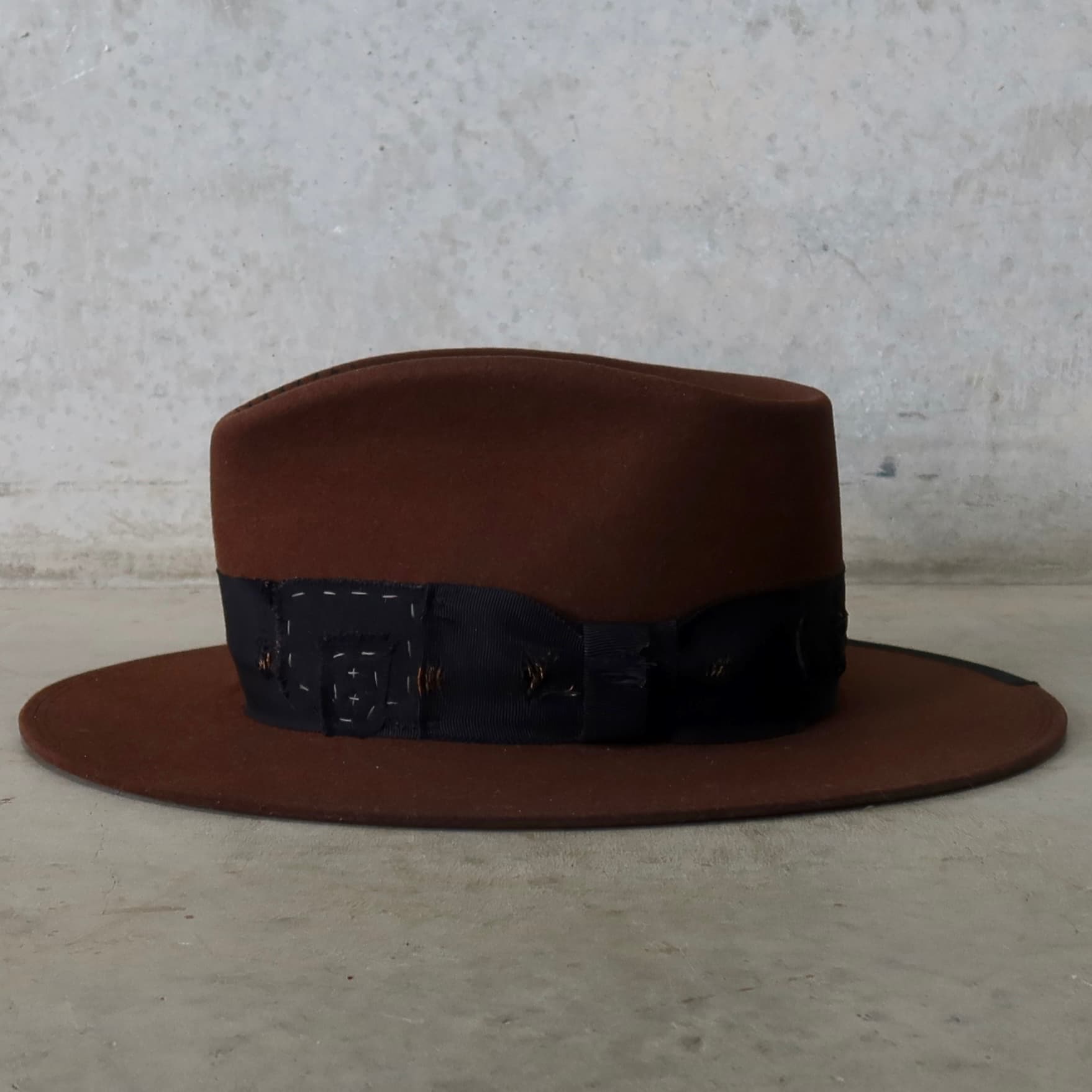 Left side view of the chocolate felt hat Brenner Limited Edition by PHYLLi Designs with distressed grosgrain band and worn fabric patches.