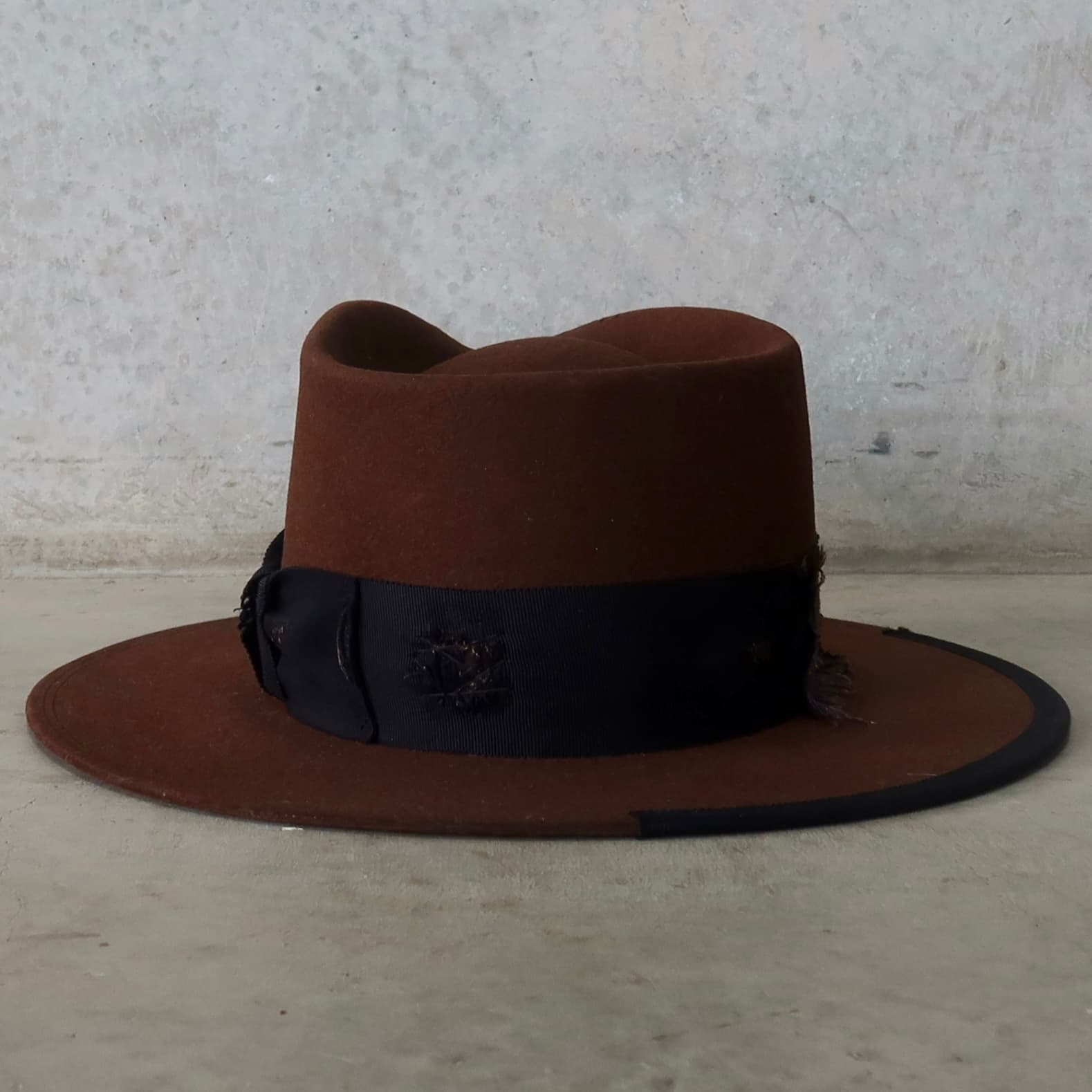 Back view of the chocolate felt hat Brenner Limited Edition by PHYLLi Designs featuring distressed patchwork trims and black grosgrain bow band.