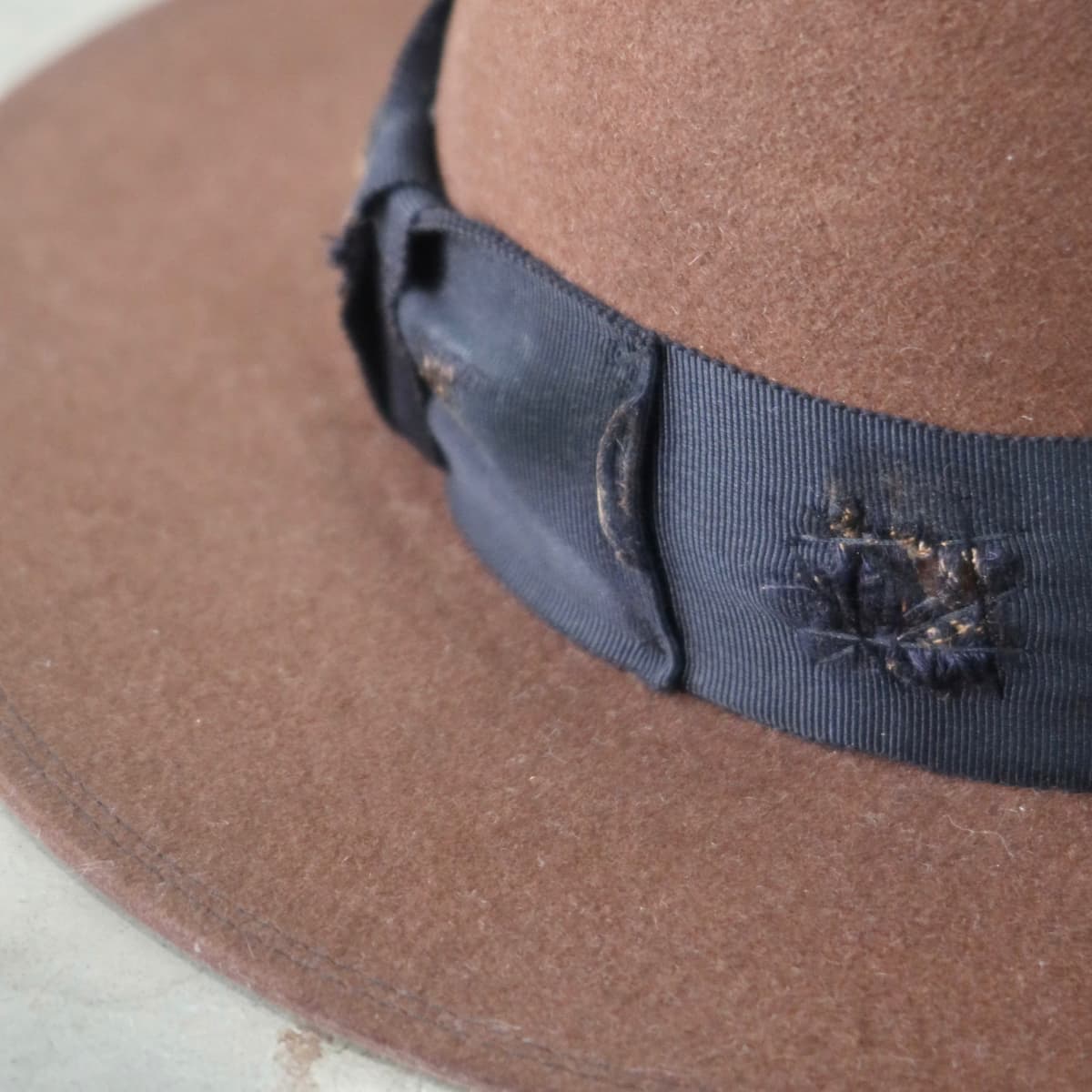 Close up detail of the Brenner Limited Edition felt hat showing distressed grosgrain bow band and worn texture.