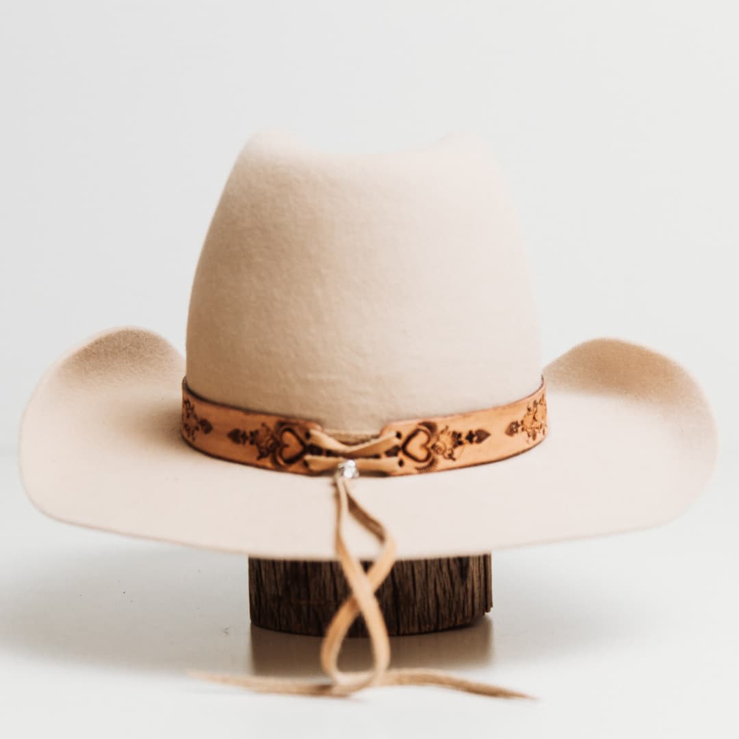 Back view of the Phylli x Buffalo Girl Palamino Heart Concho Hat Band featuring smoke deer hide lace tie back detail on a beige felt cowboy hat by PHYLLi Designs.