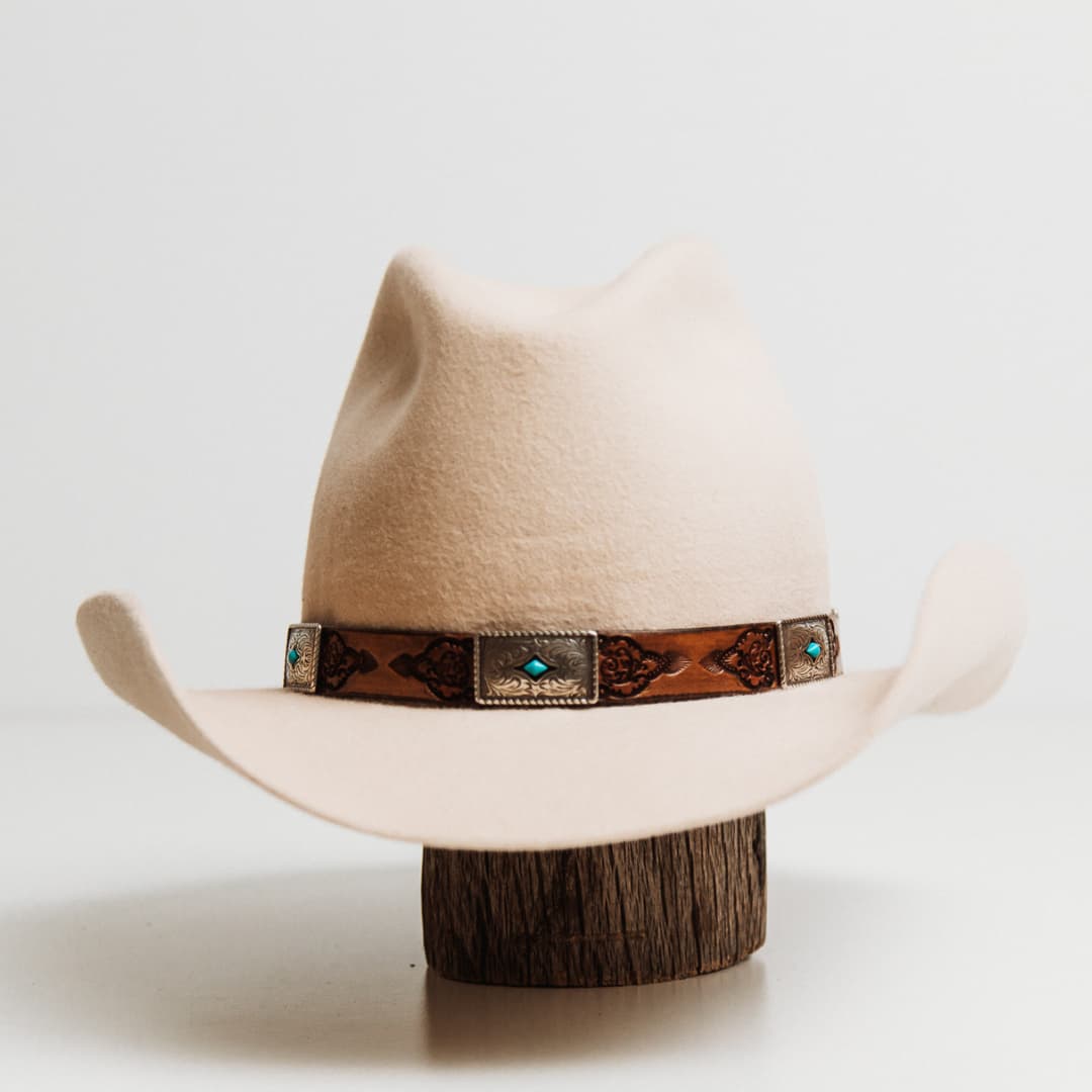 PHYLLi x Buffalo Girl Rugged Desert Buckle Hat Band with antique brown hand tooled leather hat band featuring five turquoise conchos on a beige felt cowboy hat by PHYLLi Designs.