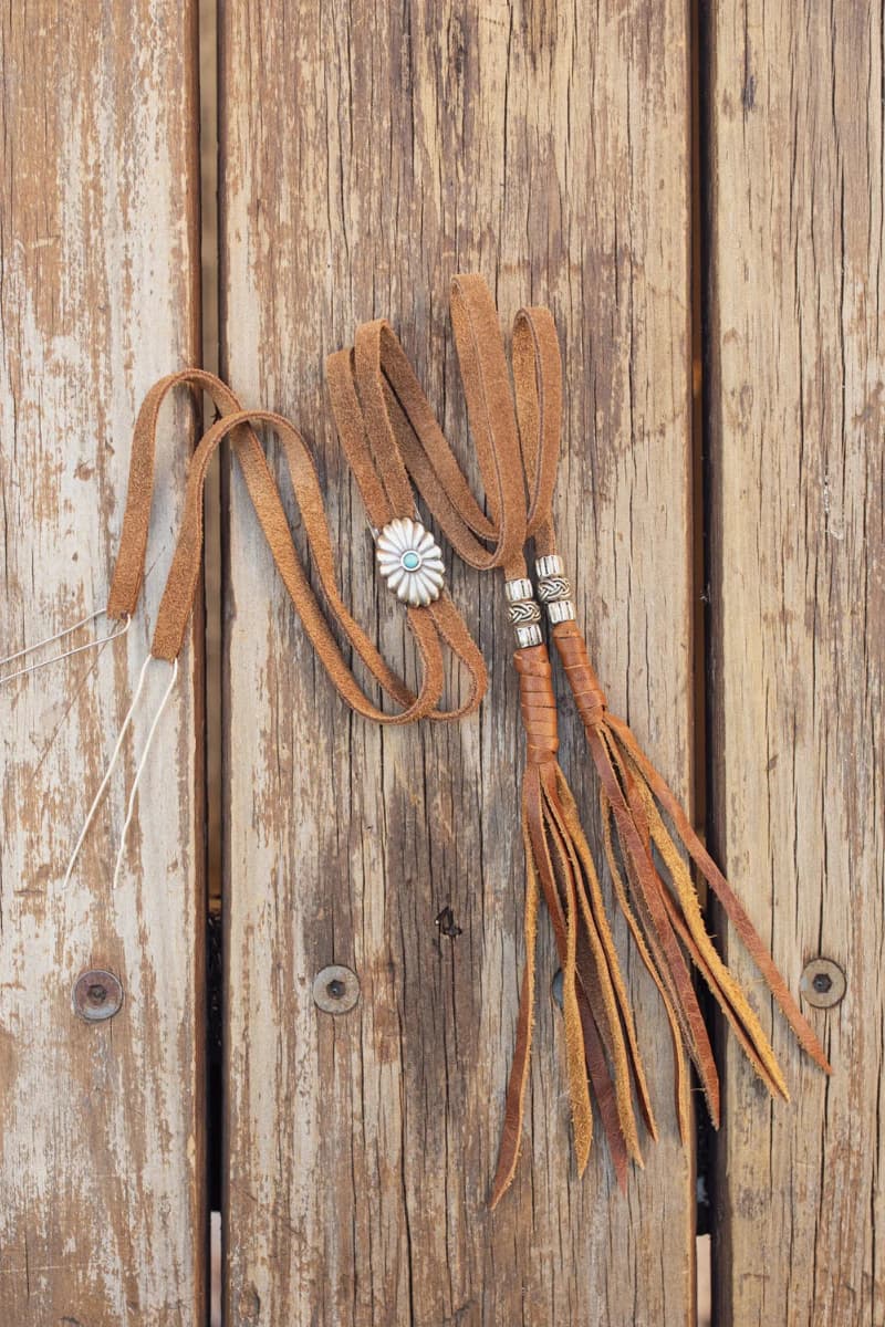 PHYLLi x Buffalo Girl Stampede Strap in tan suede displayed flat on rustic timber boards showing attachment wire, concho slider and tassel ends.