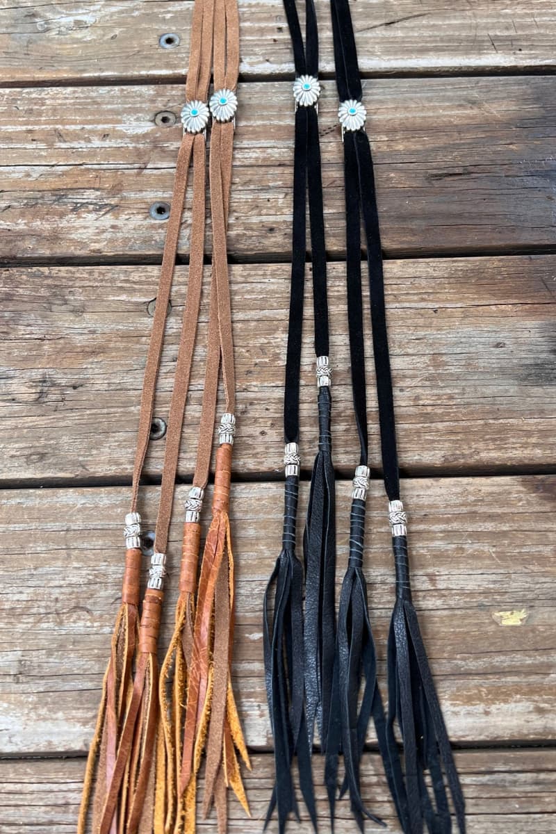 Tan and black PHYLLi x Buffalo Girl Stampede Straps displayed side by side showing suede cords, concho slider and leather tassel ends.
