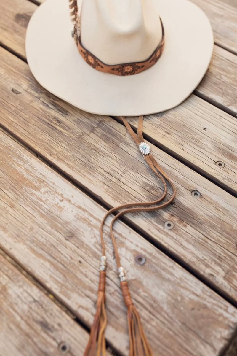 Tan suede PHYLLi x Buffalo Girl Stampede Strap featuring silver concho adjuster and leather tassel ends with bead detailing.