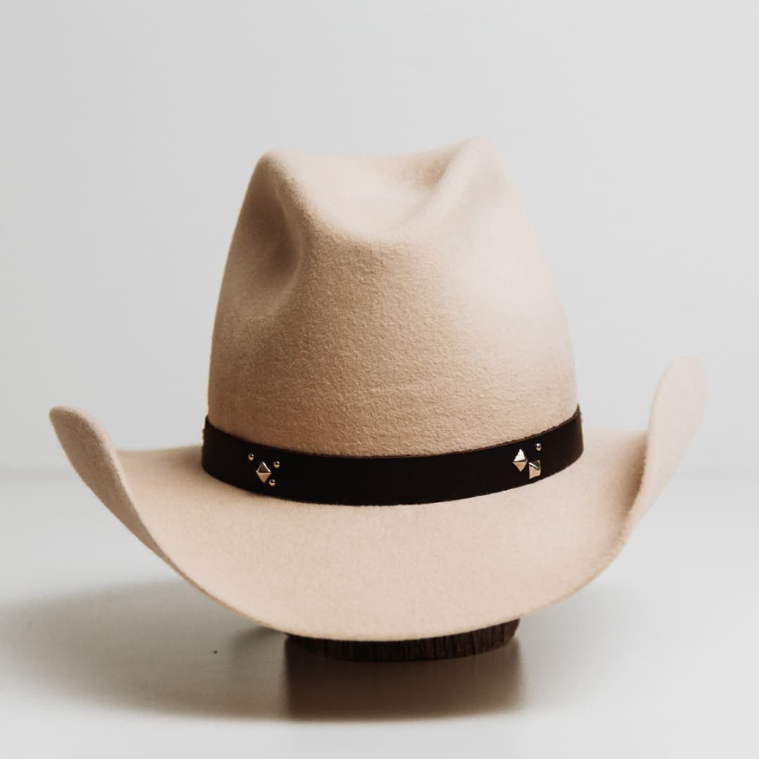 Buffalo Tieback Studded Hat Band featuring dark brown buffalo hide band with stainless steel studded detailing on a beige felt cowboy hat by PHYLLi Designs.