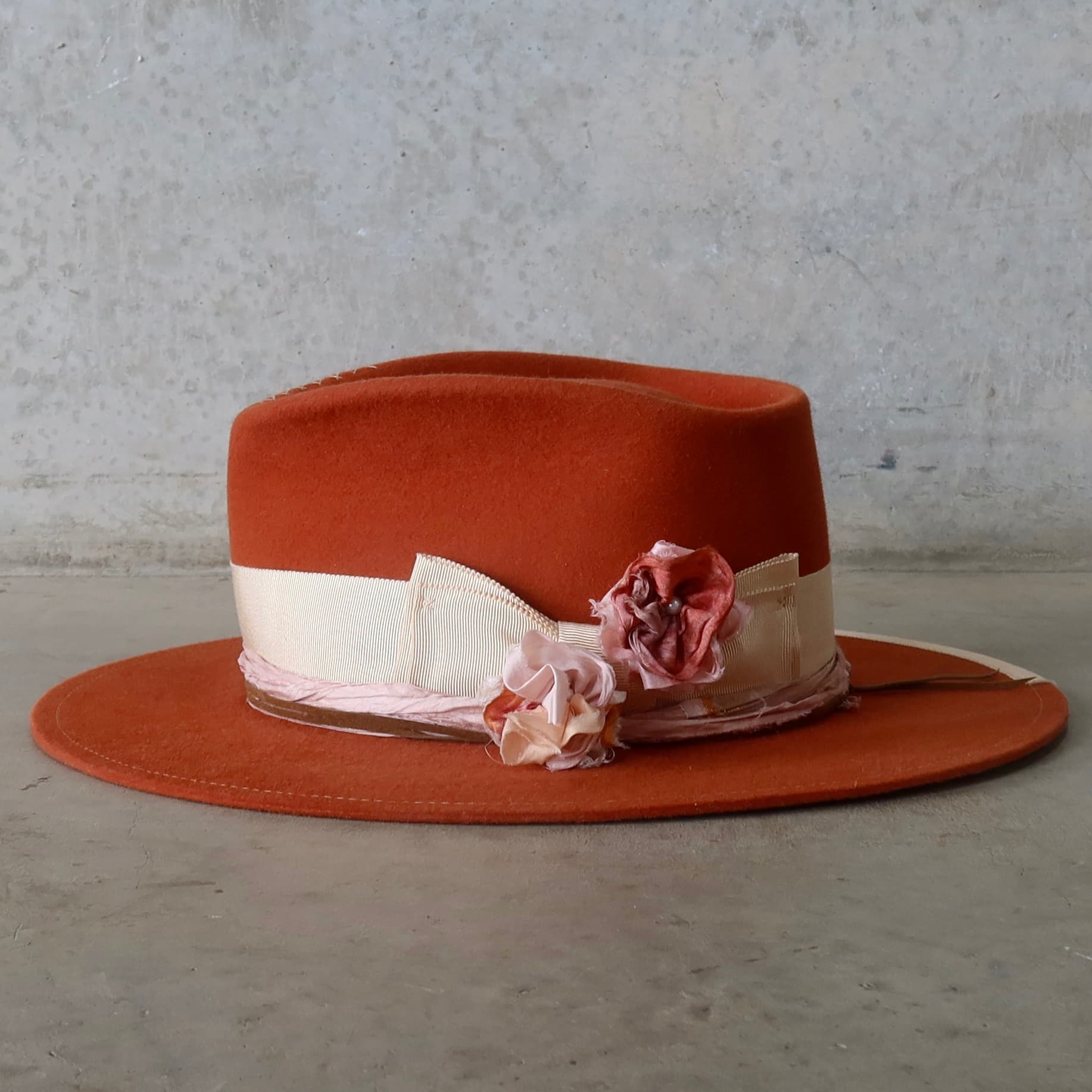 Left side view of the Spiced Pumpkin felt hat Canna by PHYLLi Designs with sand grosgrain band and removable sari silk lapel blooms.