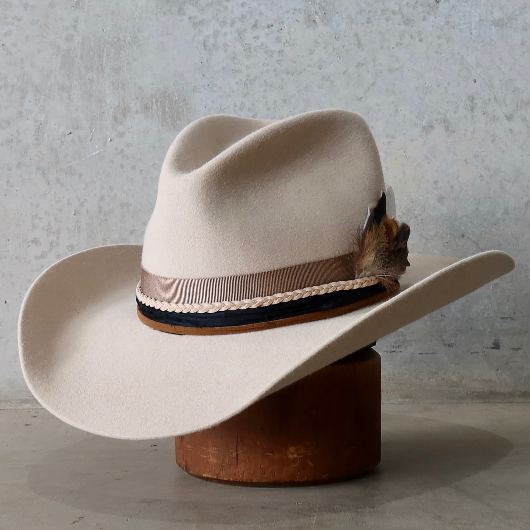Front left angle of the beige felt cowboy hat Casey Beige by PHYLLi Designs showcasing the taupe grosgrain band, black sari silk trim and plaited nude suede tie at the back.
