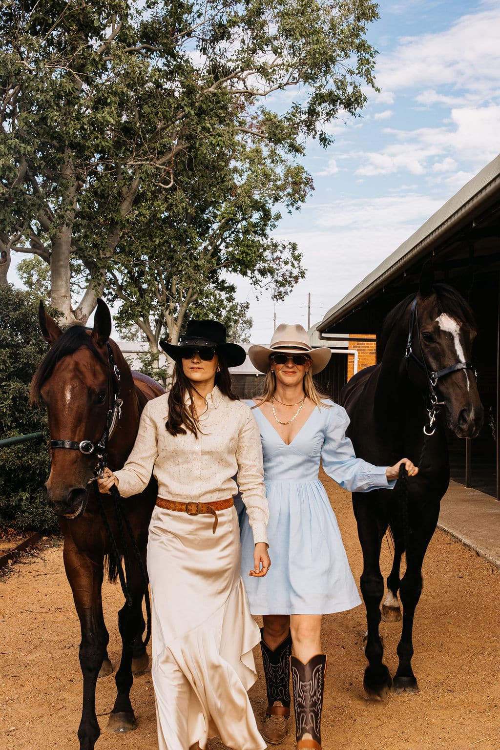 Woman wearing the PHYLLi Casey Beige felt hat with a light blue dress and cowboy boots, leading a horse in a rural Australian setting.