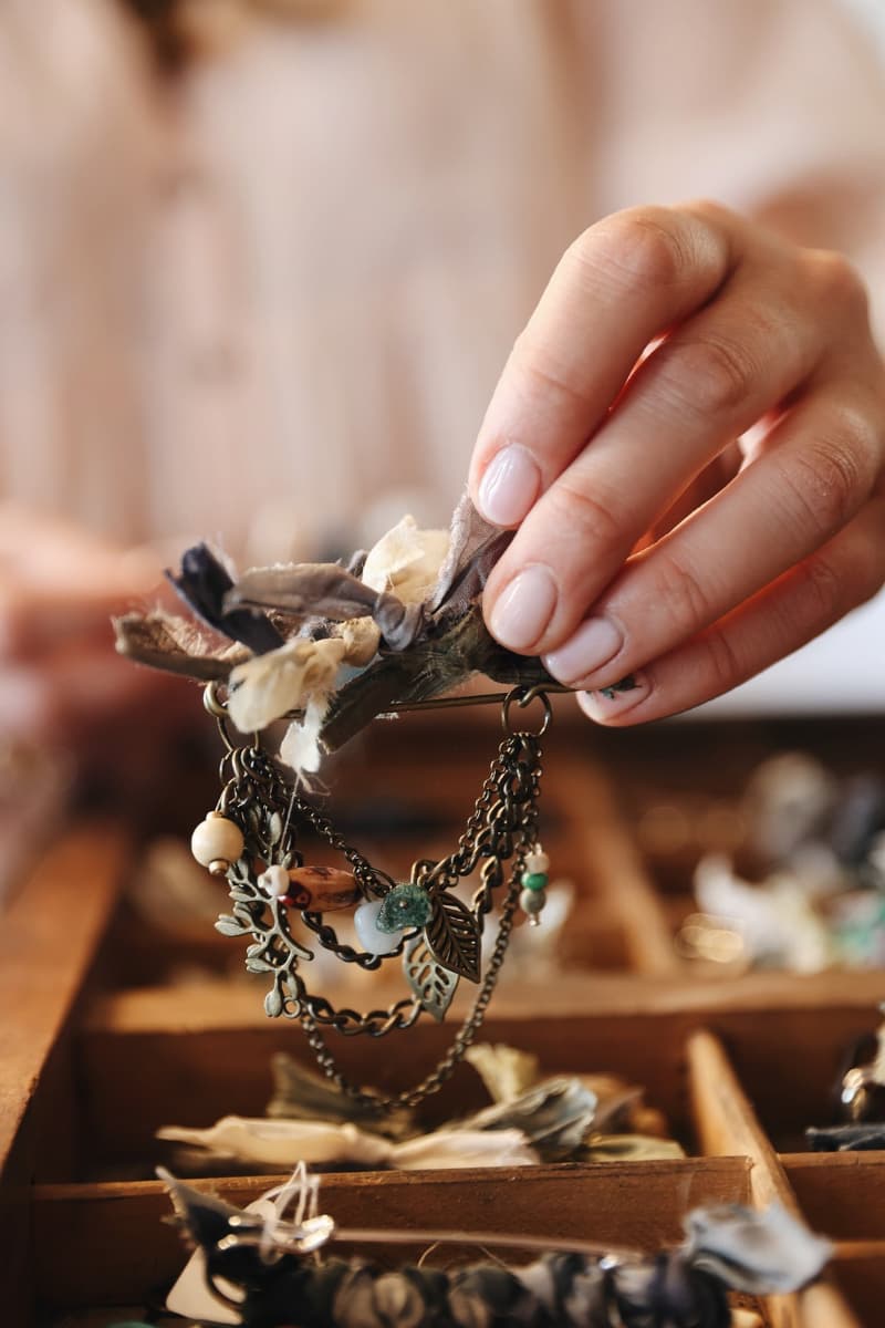 Close up detail of a chunky hat pin being held by hand above a wooden hatmaking tray in a studio setting.