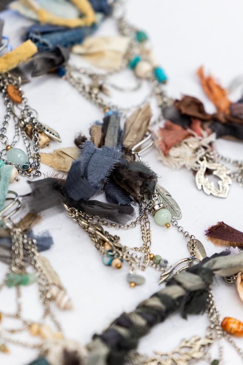 Close up detail of chunky hat pins showing blue and neutral sari silk ribbons with silver chains, turquoise beads and feather charms.