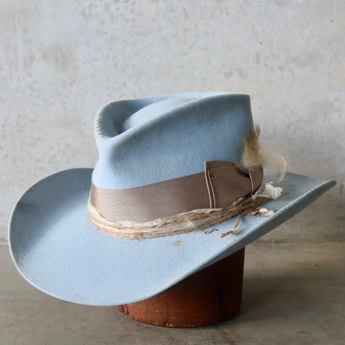 Front left angle of the Crystal Blue felt cowboy hat Clareville Limited Edition by PHYLLi Designs with taupe Japanese grosgrain bow band, twine wraps and feather trim.