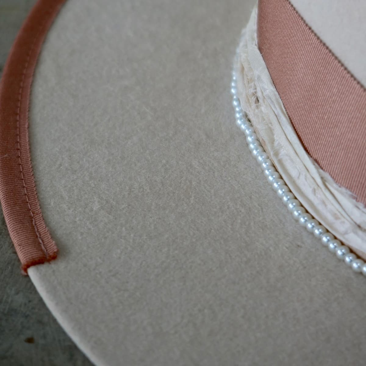 Close up detail of the Clementine felt hat showing dirty rose Japanese grosgrain brim trim, sorbet sari silk trimming and glass pearl hat necklace.