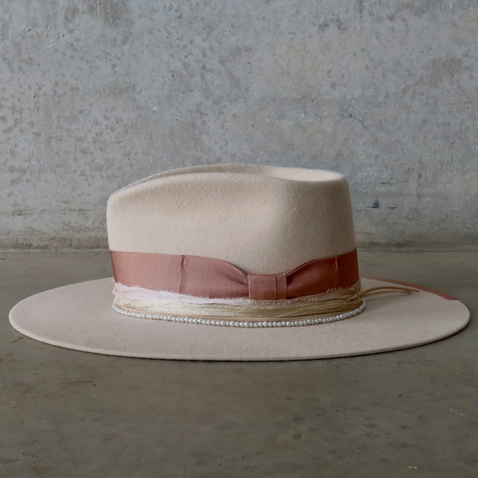 Left side view of the beige felt hat Clementine by PHYLLi Designs with sorbet sari silk trimming and glass pearl hat necklace.