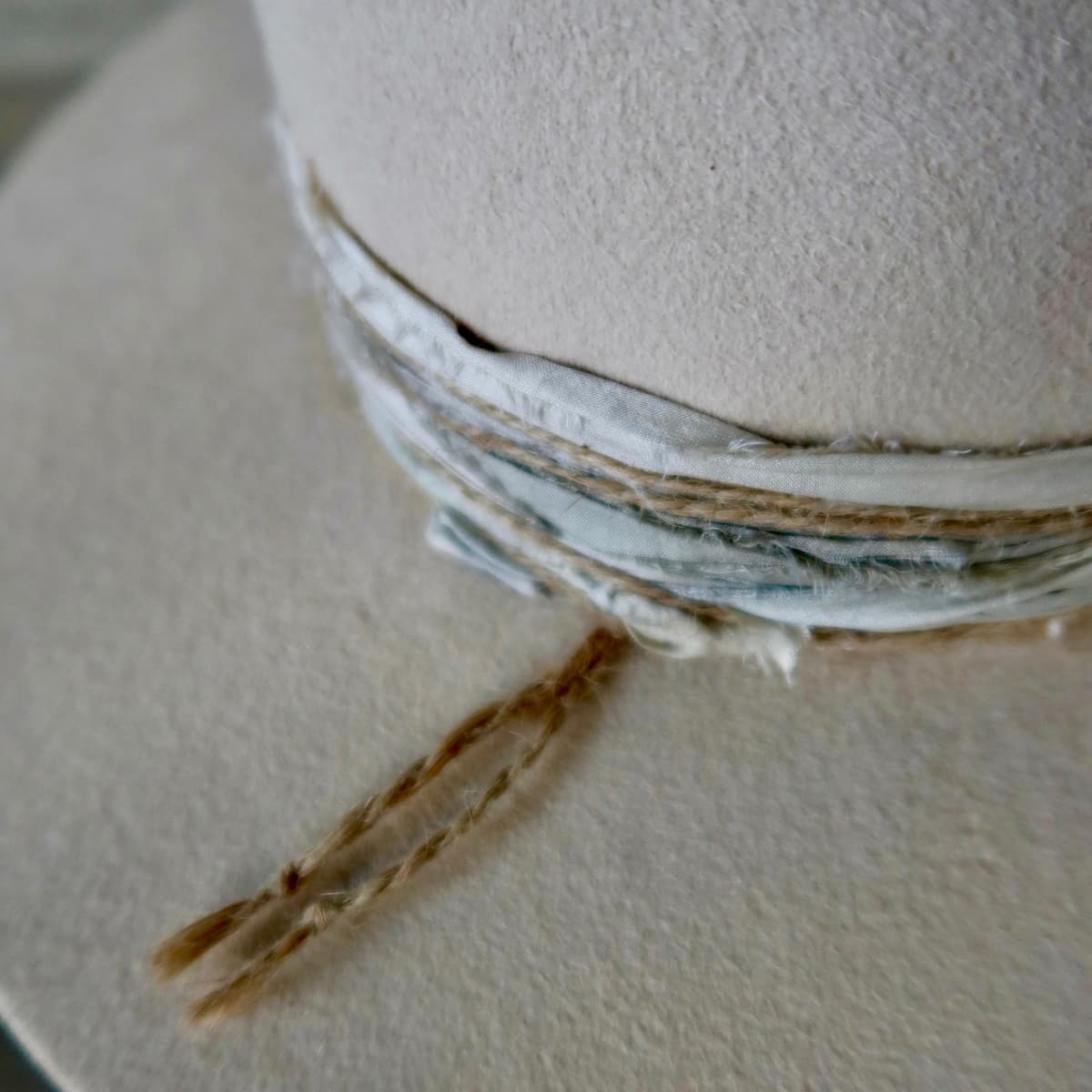 Close up detail of the Coastline felt hat showing sand and blue tie-dye sari silk trims layered beneath the band.