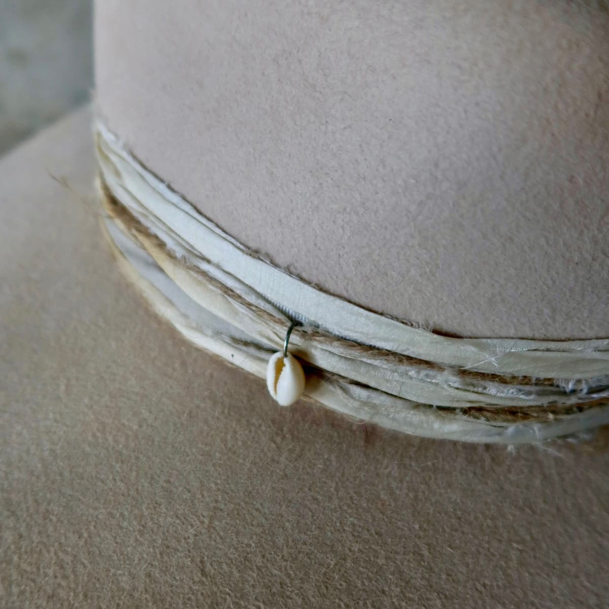 Close up detail of the Coastline felt hat showing cowrie shell charm set into the twine wraps.