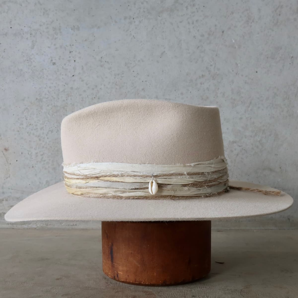 Left side view of the beige felt hat Coastline by PHYLLi Designs with five twine wraps and cowrie shell detail.