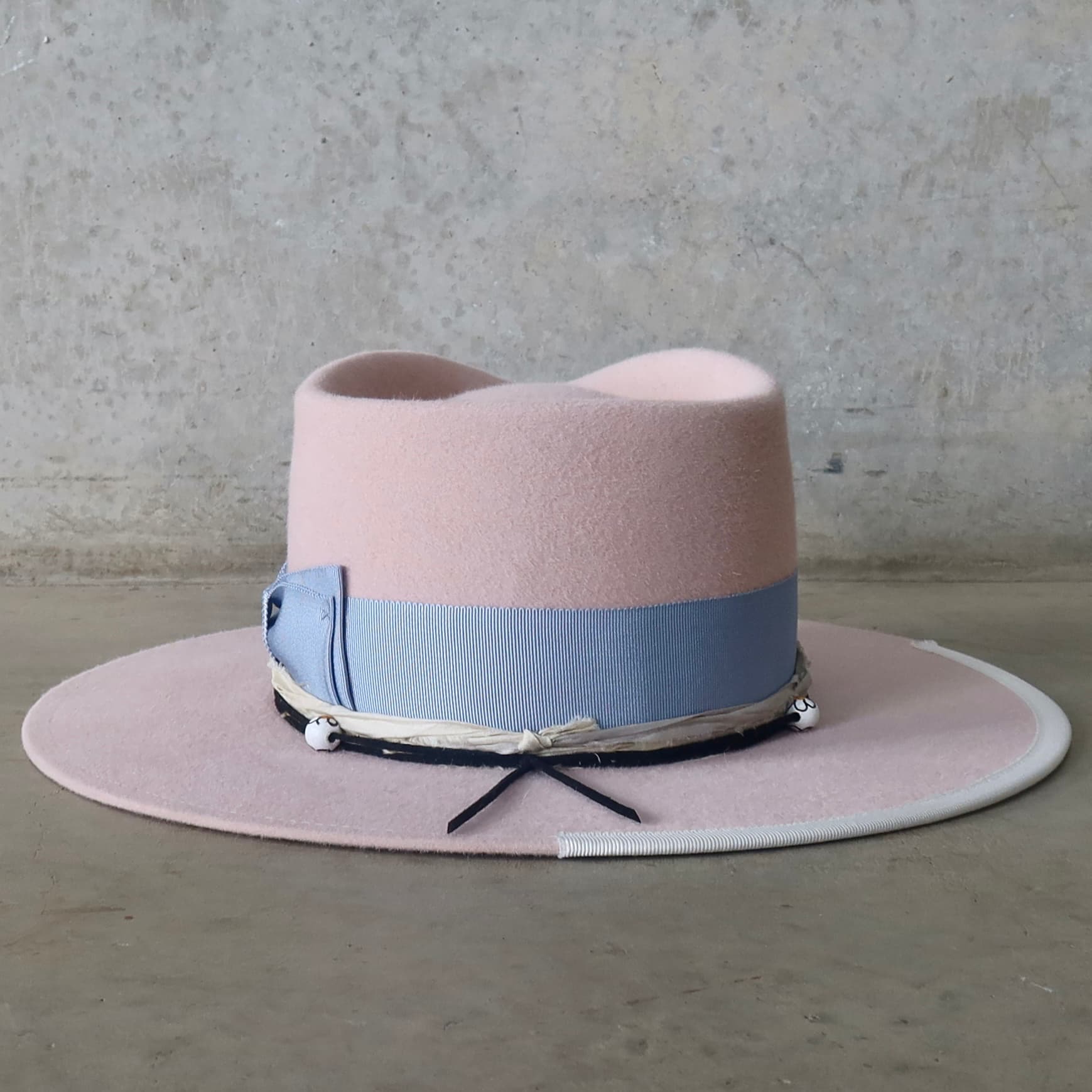 Back view of the baby pink felt hat Daisy by PHYLLi Designs with black suede string and hand-painted daisy beads.