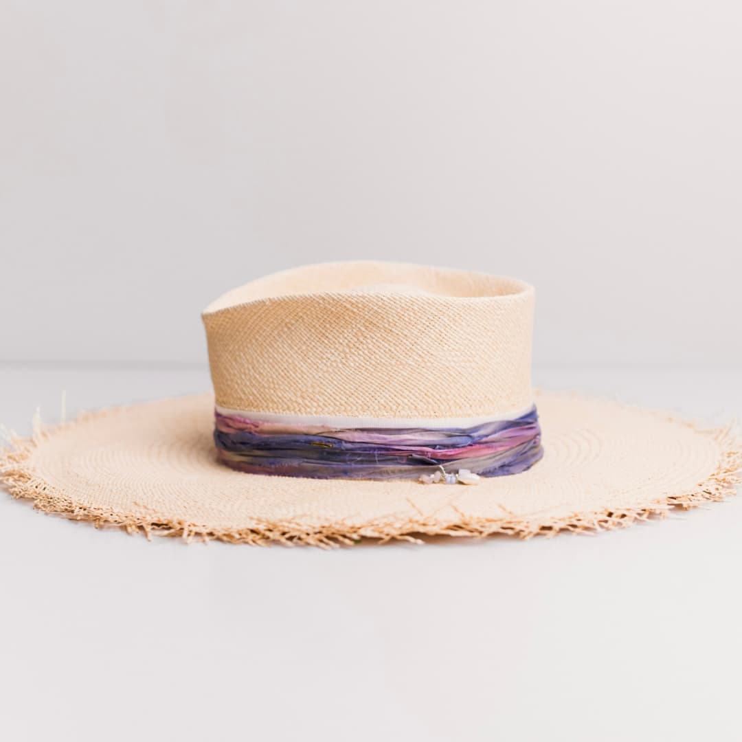 Left side view of the natural Panama straw hat Delfina by PHYLLi Designs with sari silk trimming and pearl, shell and rose quartz charm cluster.