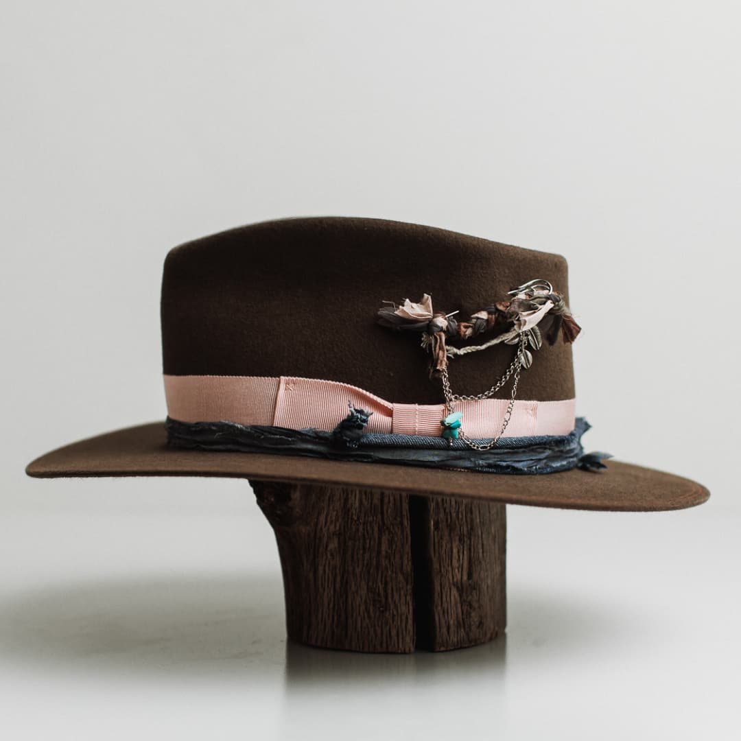 Left side view of the Denman dirty olive felt hat by PHYLLi Designs with sherbet pink grosgrain band and silver chunky hat pin with charms.