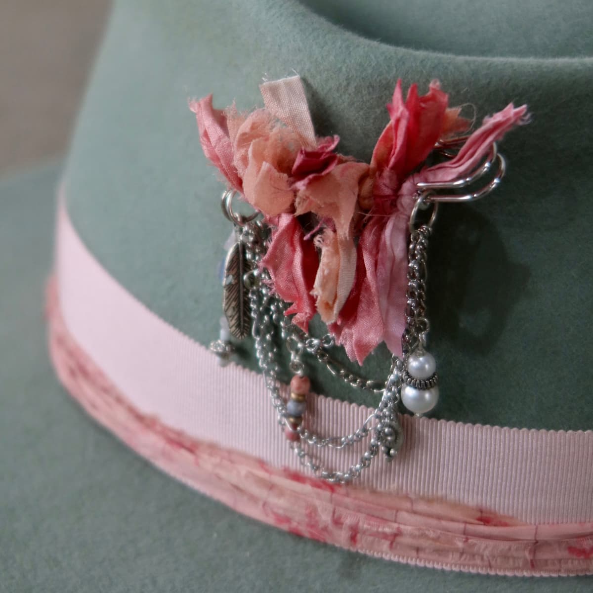 Close up detail of the Diamonds & Pearls – Pink felt hat showing silver chunky hat pin with sari silk tassels, beads and pendant chains.