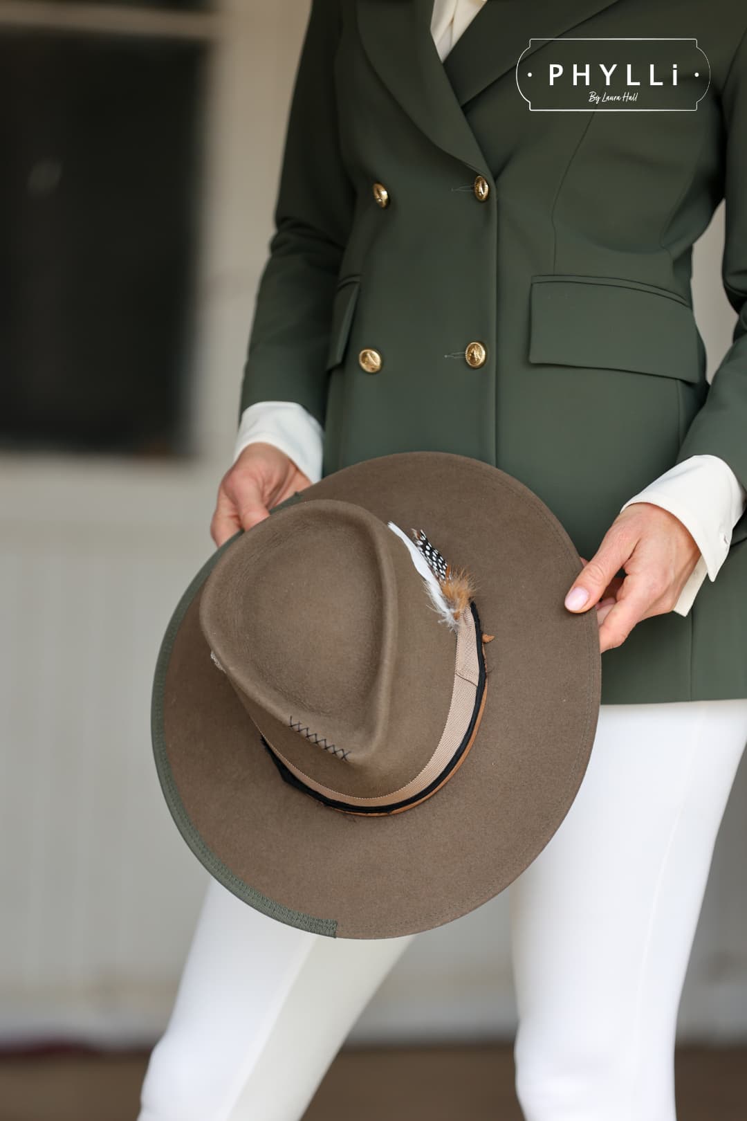 Woman dressed in equestrian clothing holding the Dirty Jane dirty olive felt hat by PHYLLi Designs featuring taupe grosgrain band, feather bunch and black sari silk trim.