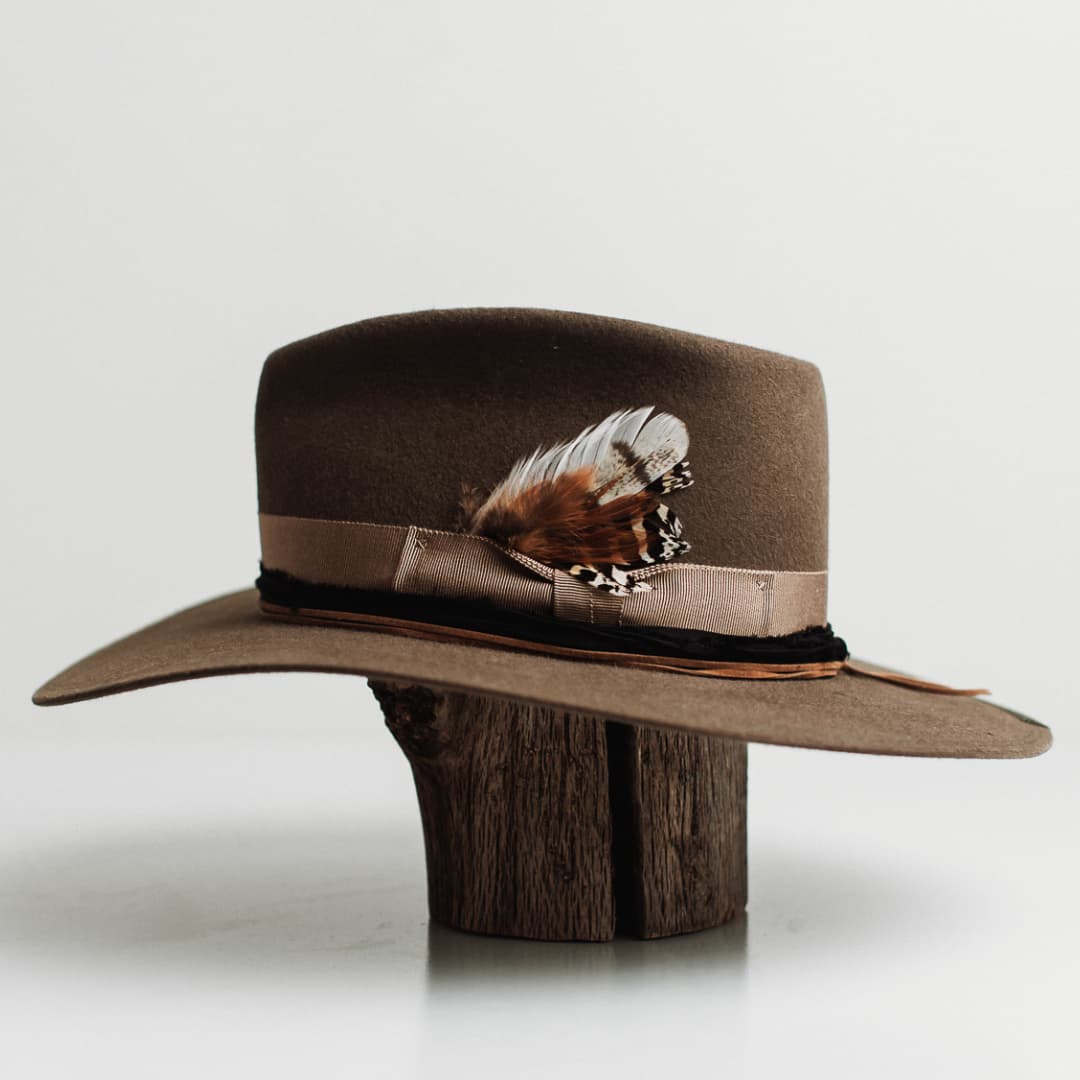 Left side view of the Dirty Jane dirty olive felt hat by PHYLLi Designs with feather bunch taupe grosgrain band and double brim stitch in dark green.