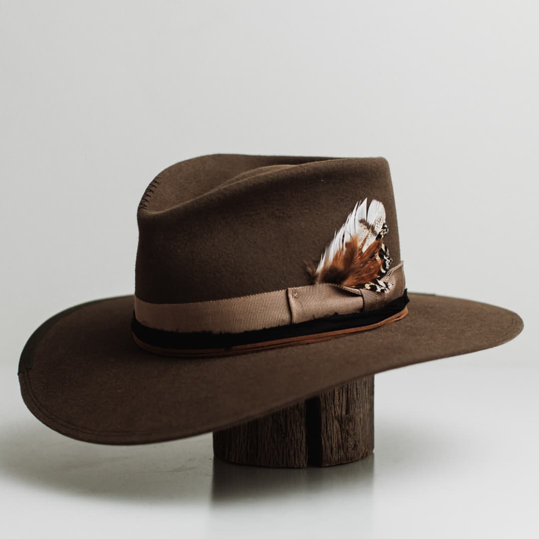 Front left angle of the Dirty Jane dirty olive felt hat by PHYLLi Designs with taupe grosgrain band, black sari silk trim and fallen feather detail.