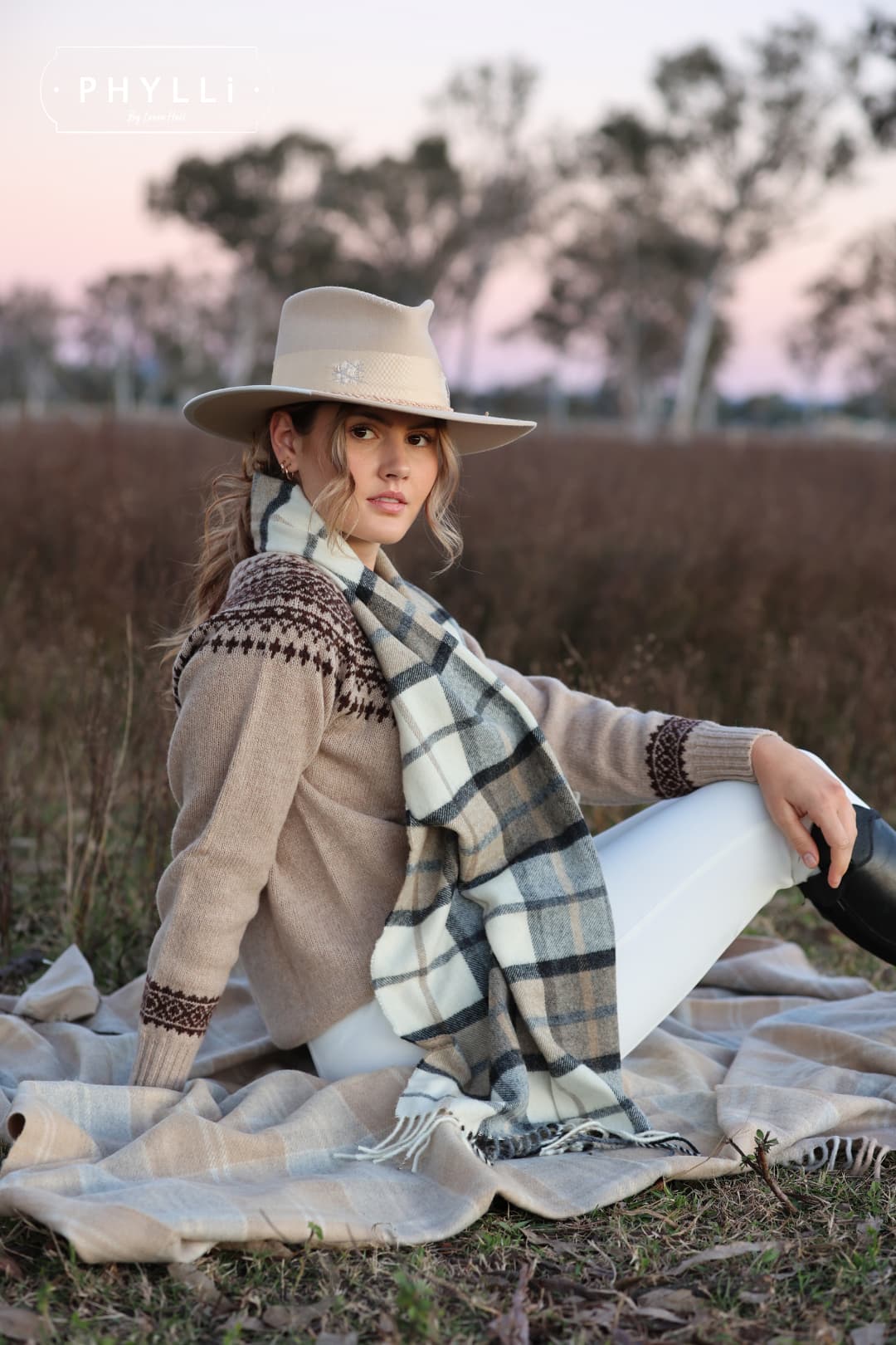 Woman wearing Fallon beige rabbit felt hat by PHYLLi Designs styled with knit sweater and plaid scarf in countryside setting.